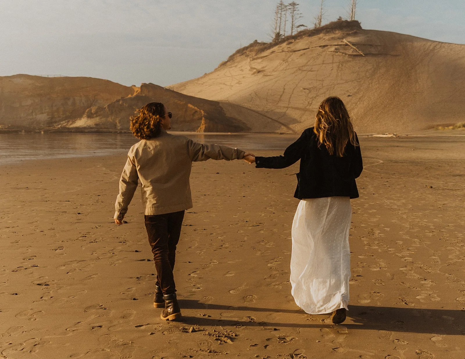 Couple walk together in the surf during their playful Cape Kiwanda engagement session on the Oregon Coast