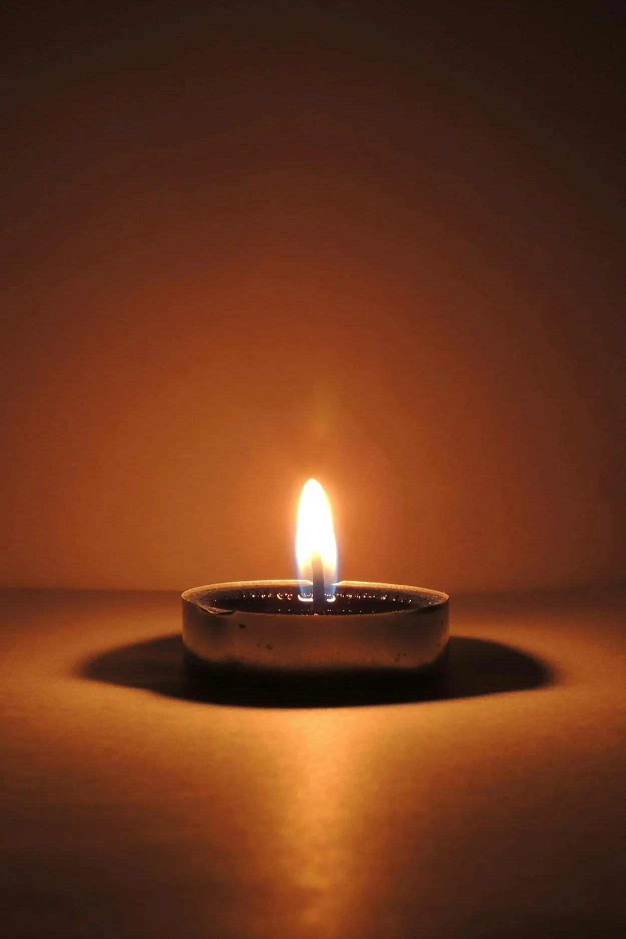 A lit candle on a flat surface with a visible flame and a dark background.