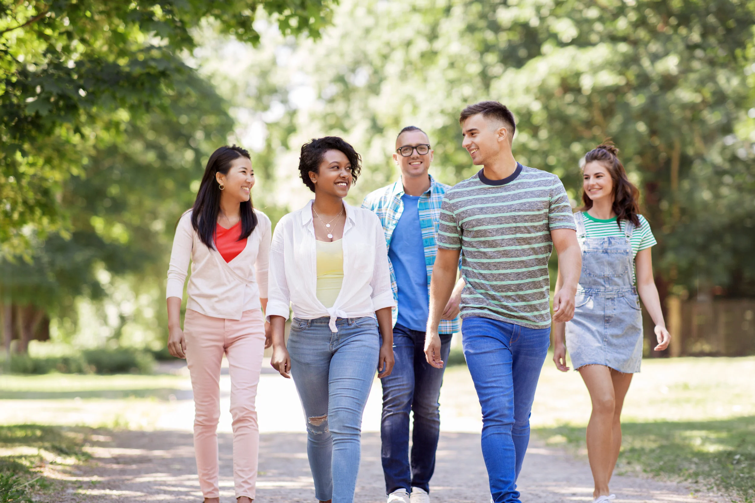 people, friendship and international concept - group of happy friends walking in park