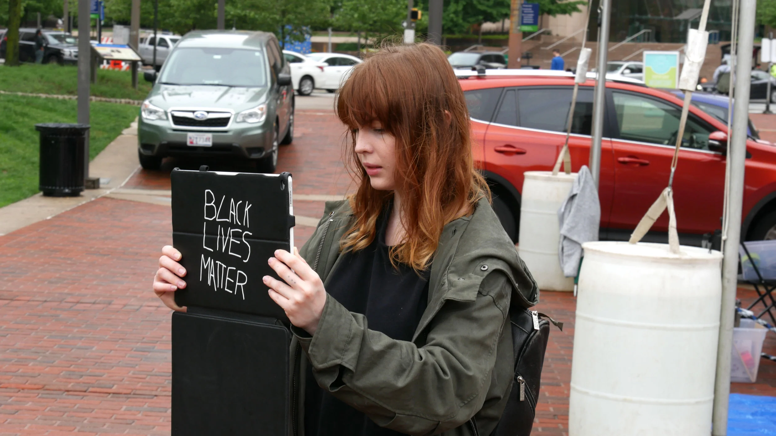 Maura Callahan holding an iPad like a protest sign and bringing back McKeldin Fountain. McKeldin Square, May 19 2018. Photograph by Timothy Nohe. © nonument01.org 2018