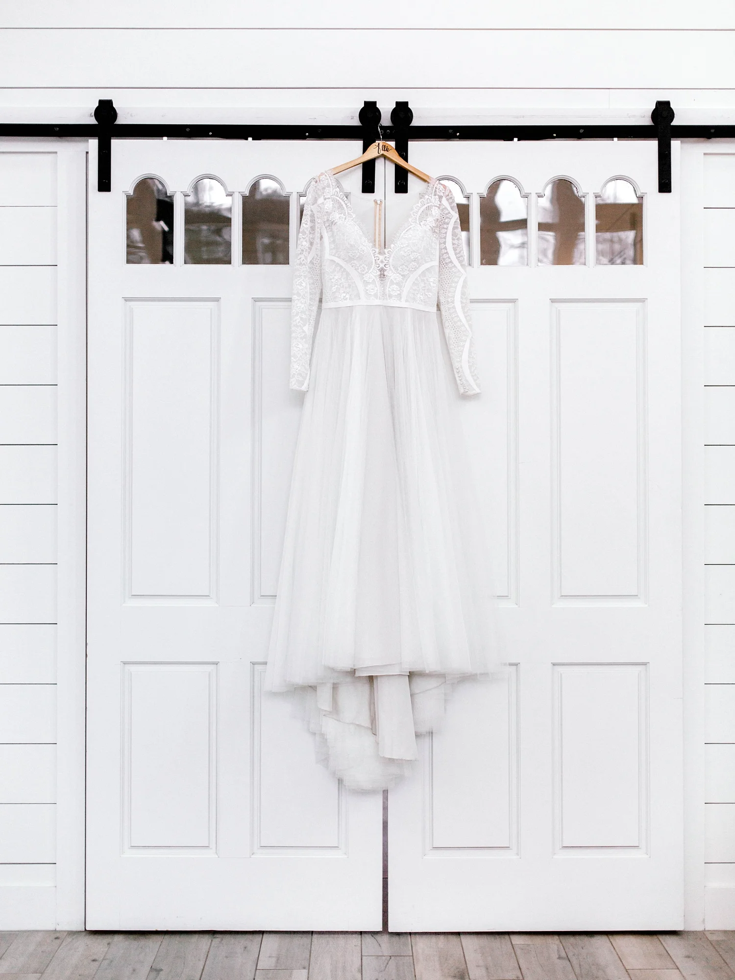 Long sleeve wedding dress hanging on white barn doors of white barn.