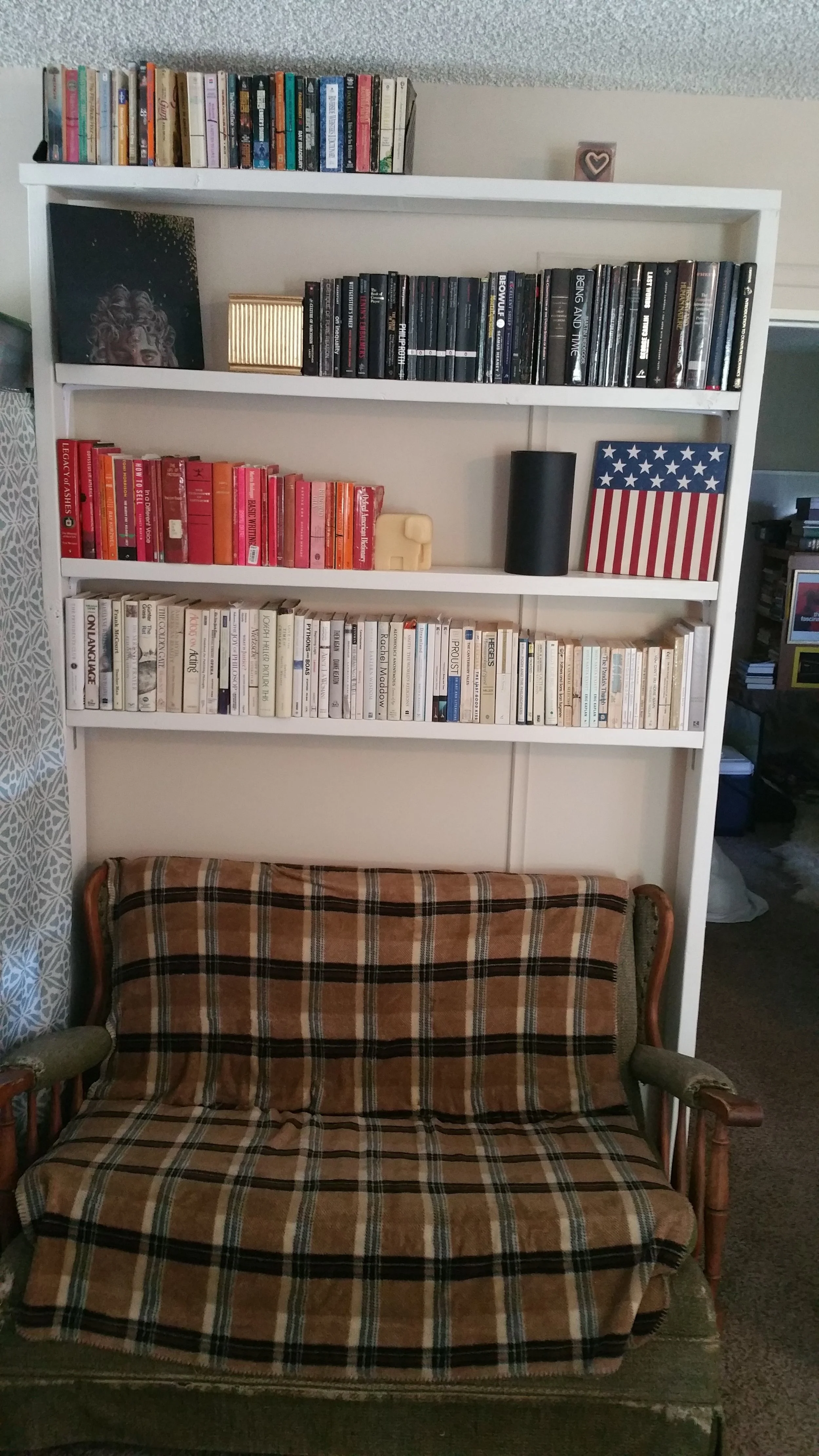 A bookshelf built by the author, volumes nicely "colored-coded" and positioned above Grandma's rocker.