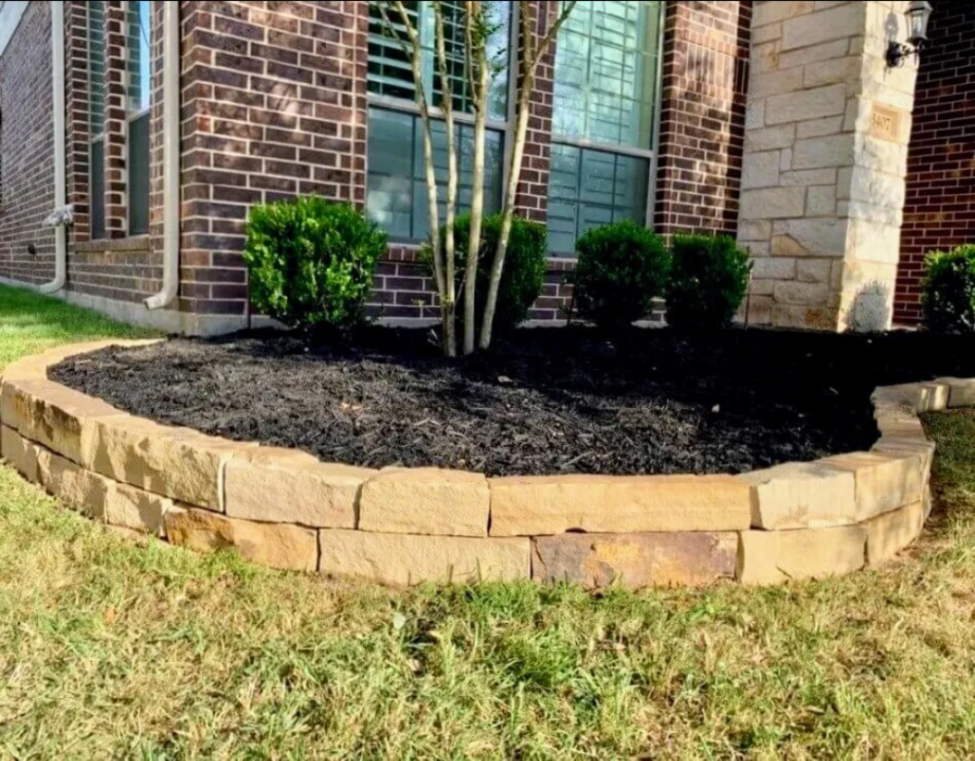 Low stone retaining wall forming a landscaped garden bed along a brick home in Northwest Arkansas, installed by ABI Systems