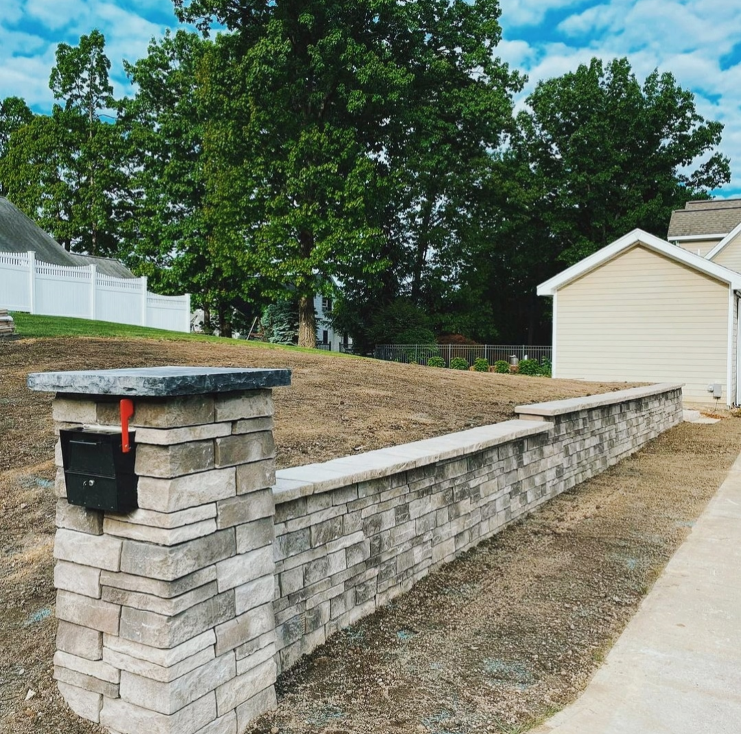 Long block retaining wall with stone mailbox column stabilizing a sloped residential yard in Northwest Arkansas, installed by ABI Systems