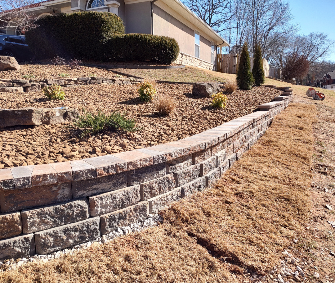 Curved block retaining wall stabilizing a sloped residential yard with rock landscaping in Northwest Arkansas, installed by ABI Systems