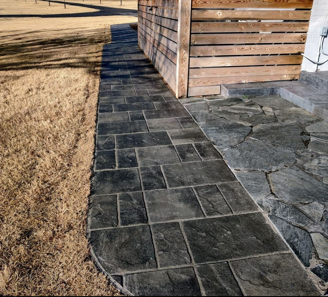 Modern paver walkway installation featuring large-format concrete pavers with a natural stone texture, designed to provide durable and low-maintenance access along the home’s exterior. This hardscape creates a clean, structured pathway while compleme