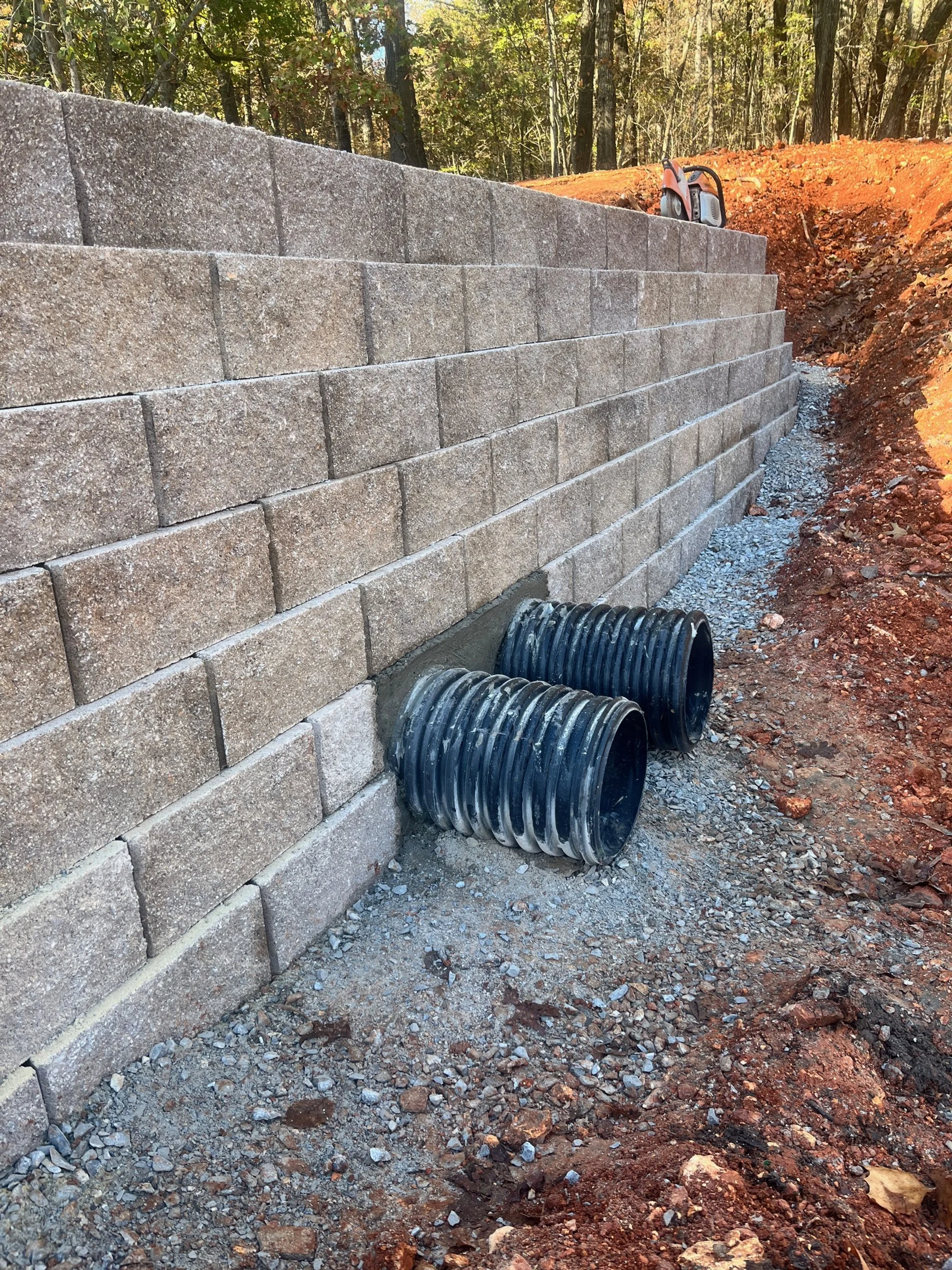 Engineered block retaining wall with integrated drainage pipes for water management and erosion control in Northwest Arkansas, installed by ABI Systems