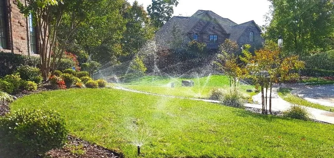 Lawn being watered by a sprinkler, with a house and trees in the background in Northwest Arkansas.