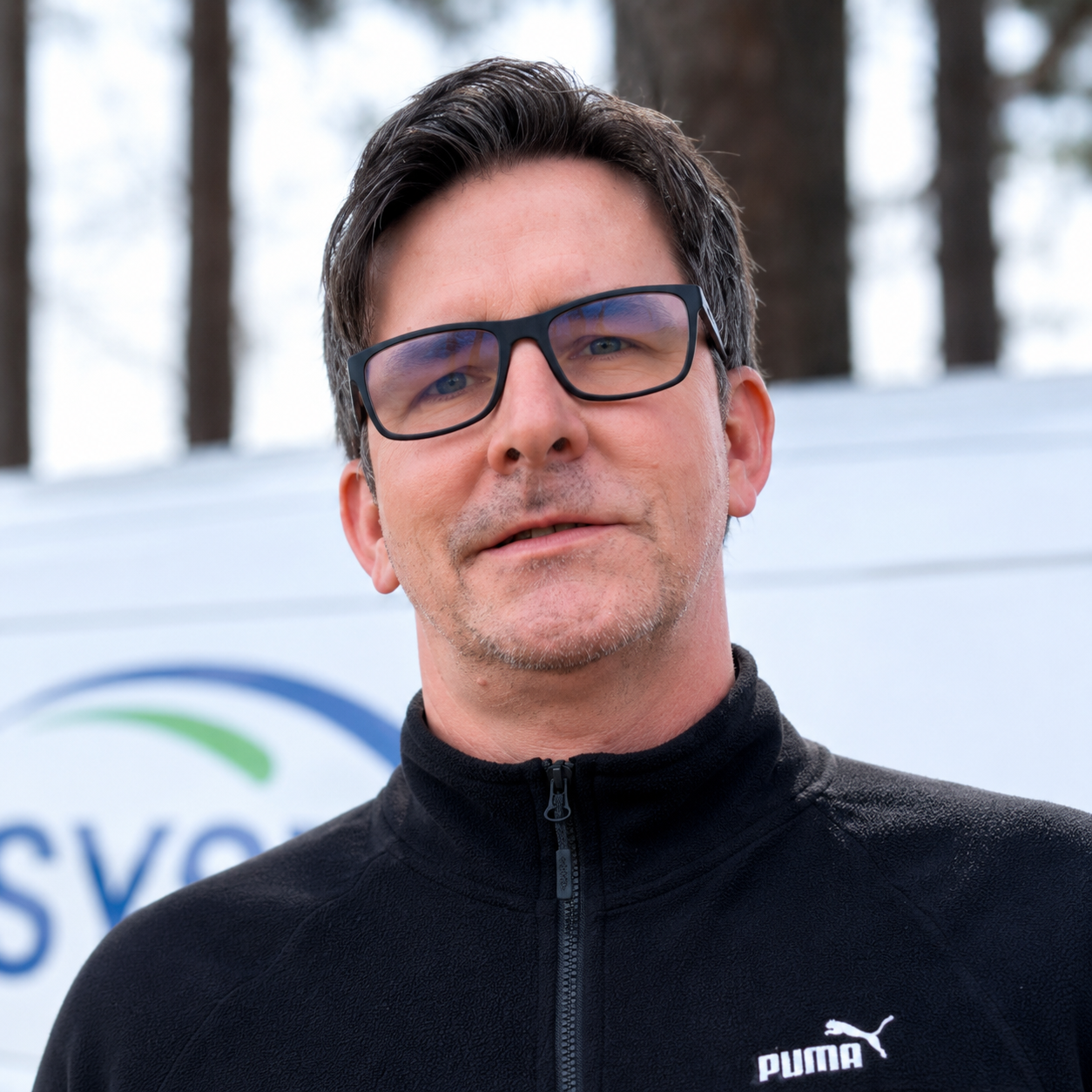 Derek Lester of ABI Systems standing outdoors in Northwest Arkansas wearing glasses and a black jacket in a professional headshot photo