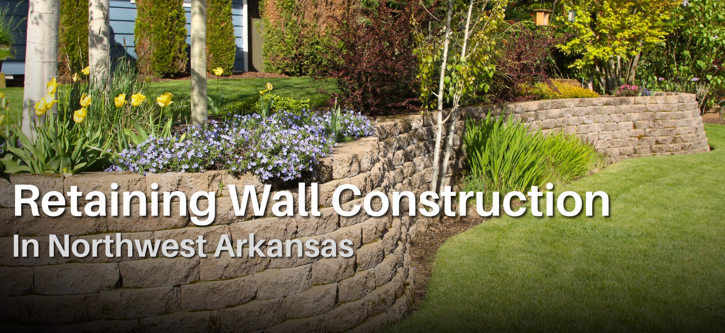 Tiered stone retaining wall with landscaped garden beds at a residential property in Northwest Arkansas, built by ABI Systems for erosion control and curb appeal