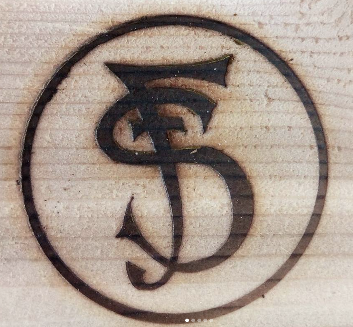 A circular metal design with a dollar sign and a pipe above it, engraved on a wooden surface.