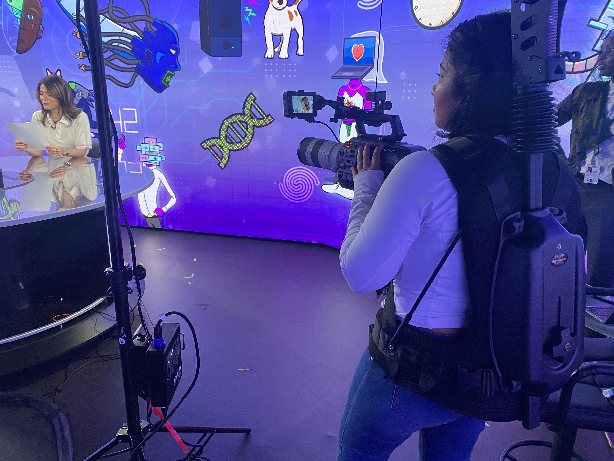 Videographer filming a presenter at a colorful technology-themed studio set.