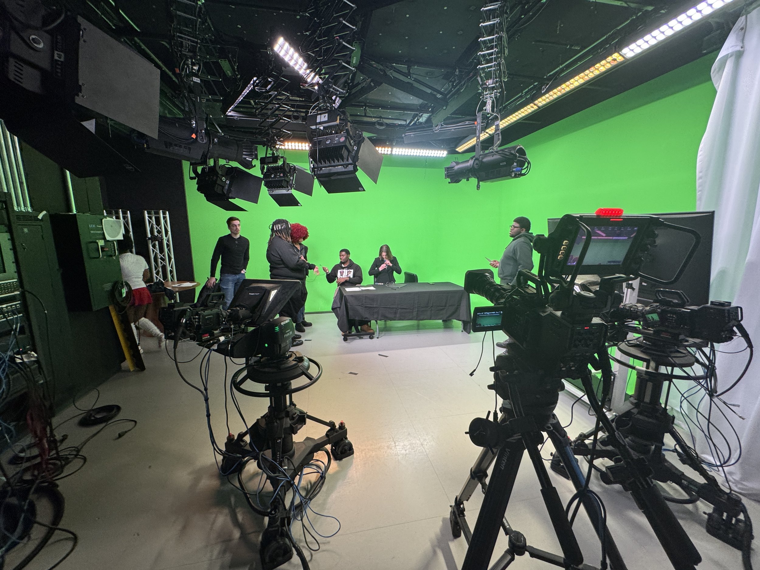 Film studio with a green screen, professional cameras, lighting equipment, and crew members on set