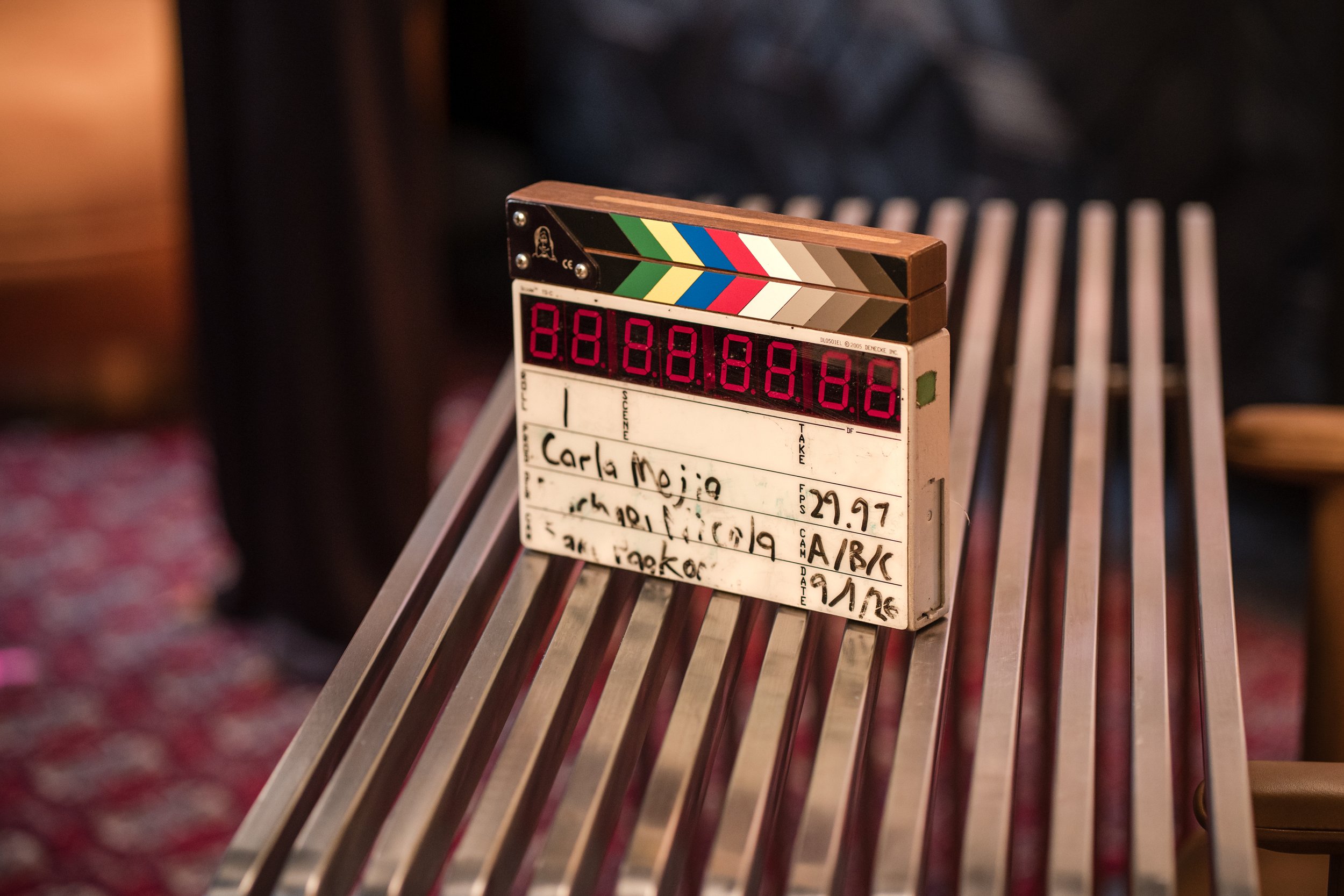 Digital film clapperboard resting on a striped chair in a production setting