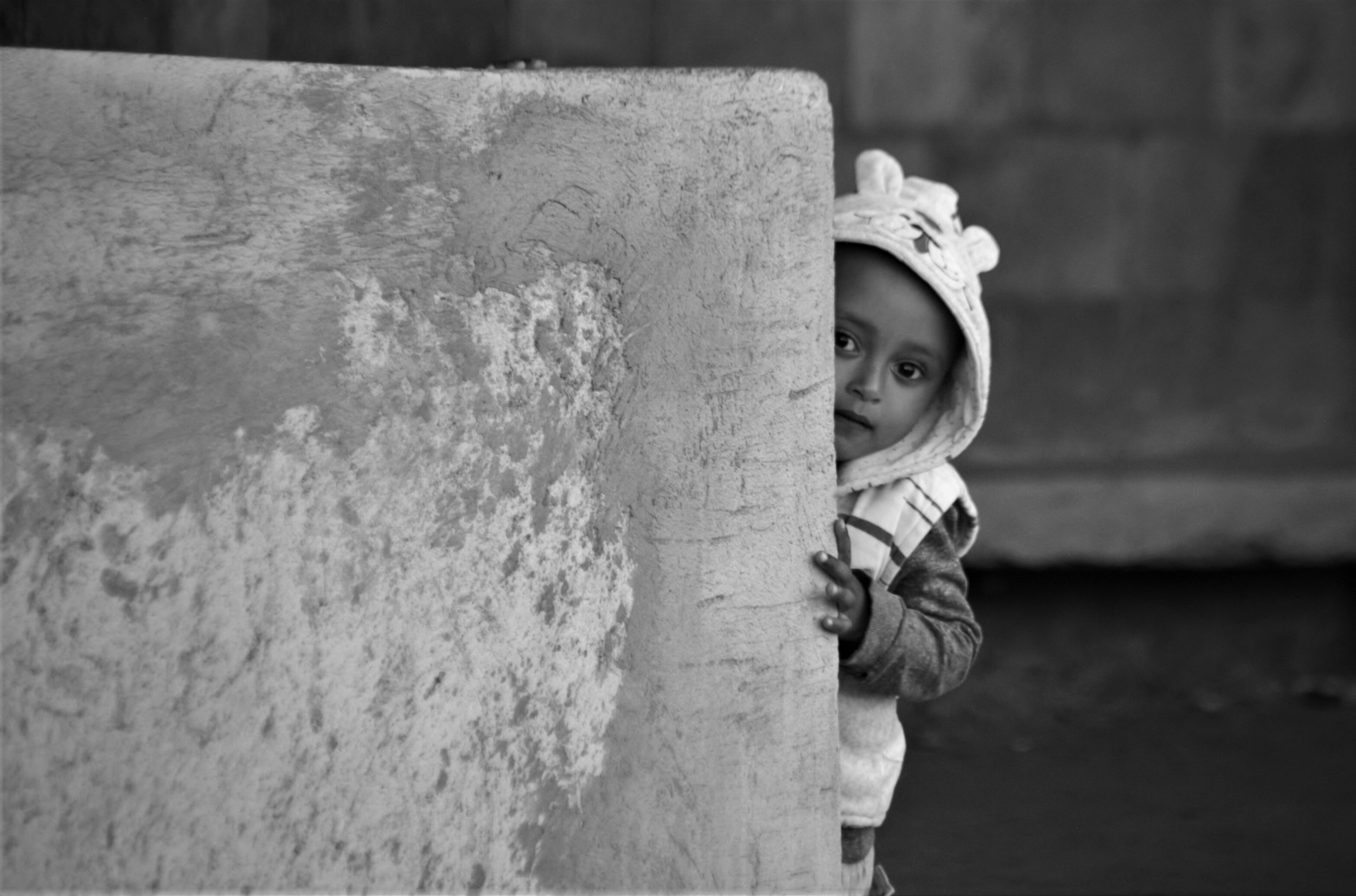 8. A young child crouches down behind a wall, eyes wide with anticipation, eagerly waiting to be found while playing hide and seek. 