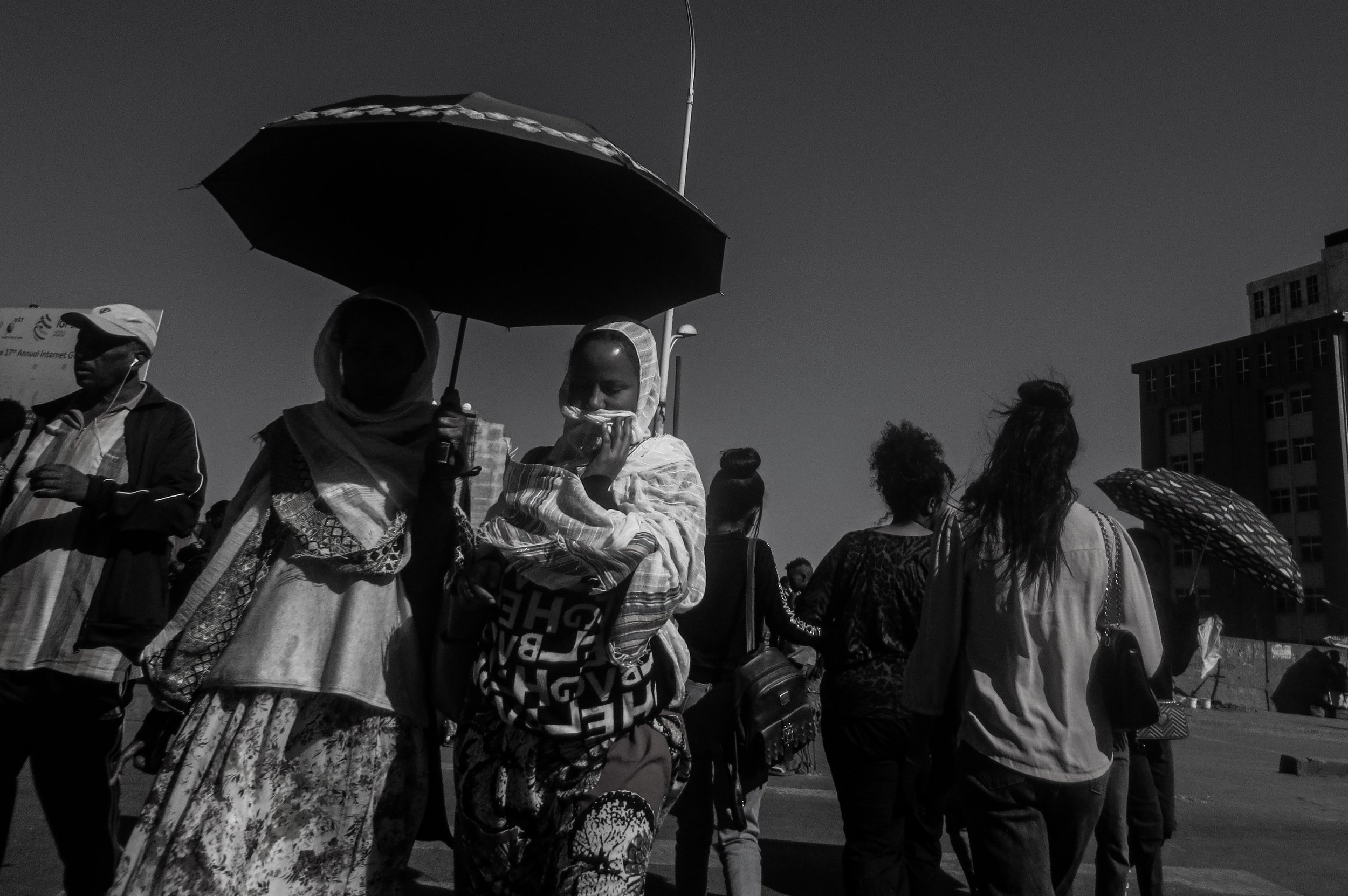  20. A group of women are seen crossing a busy street, each holding a colourful umbrella to shield themselves from the hot sun. The umbrellas add a pop of colour to the otherwise grey and damp scene. The women appear to be in a hurry, as they briskly