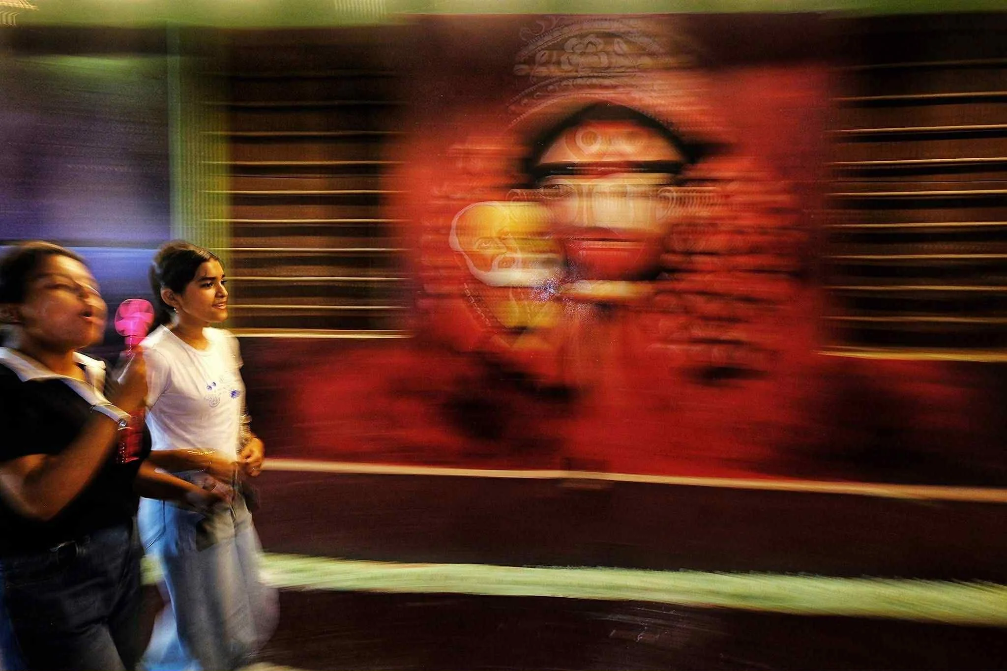 Rajib Singha - This vibrant image captures the warmth and movement of culture and society, showcasing two joyful girls in everyday activities alongside deities. It's beautiful.