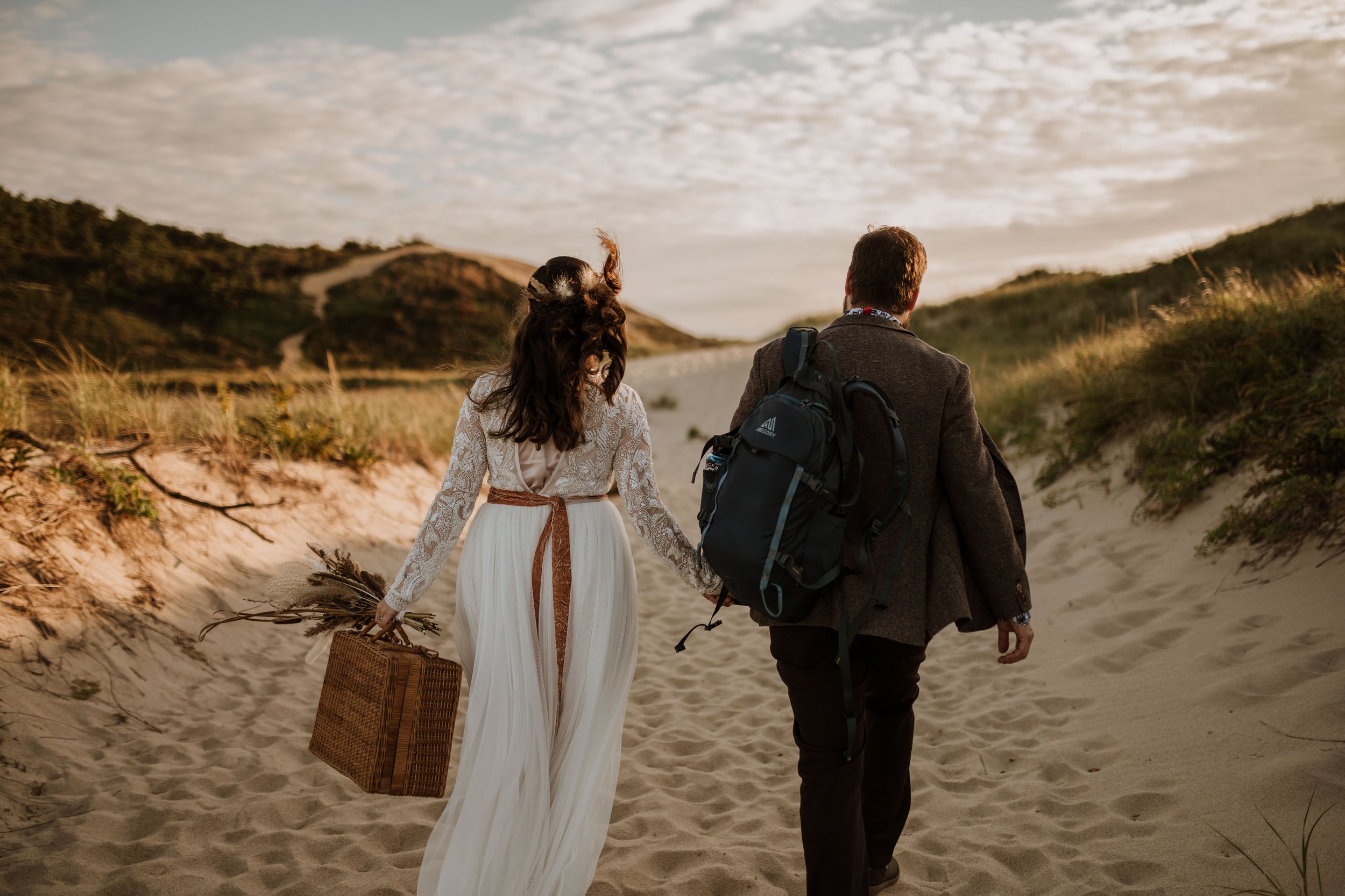 Couple walking toward the ocean along a sandy path in the dunes.