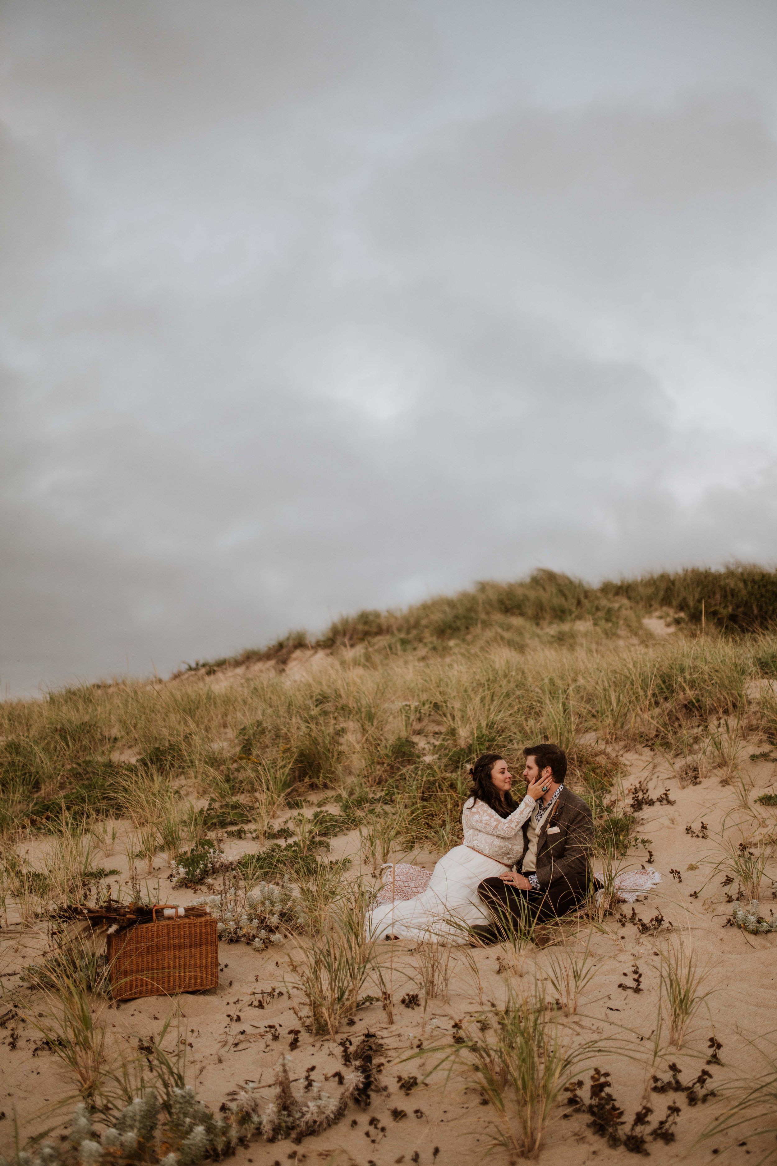 Newlywed couple sitting together in the dunes of Cape Cod National Seashore during blue hour.