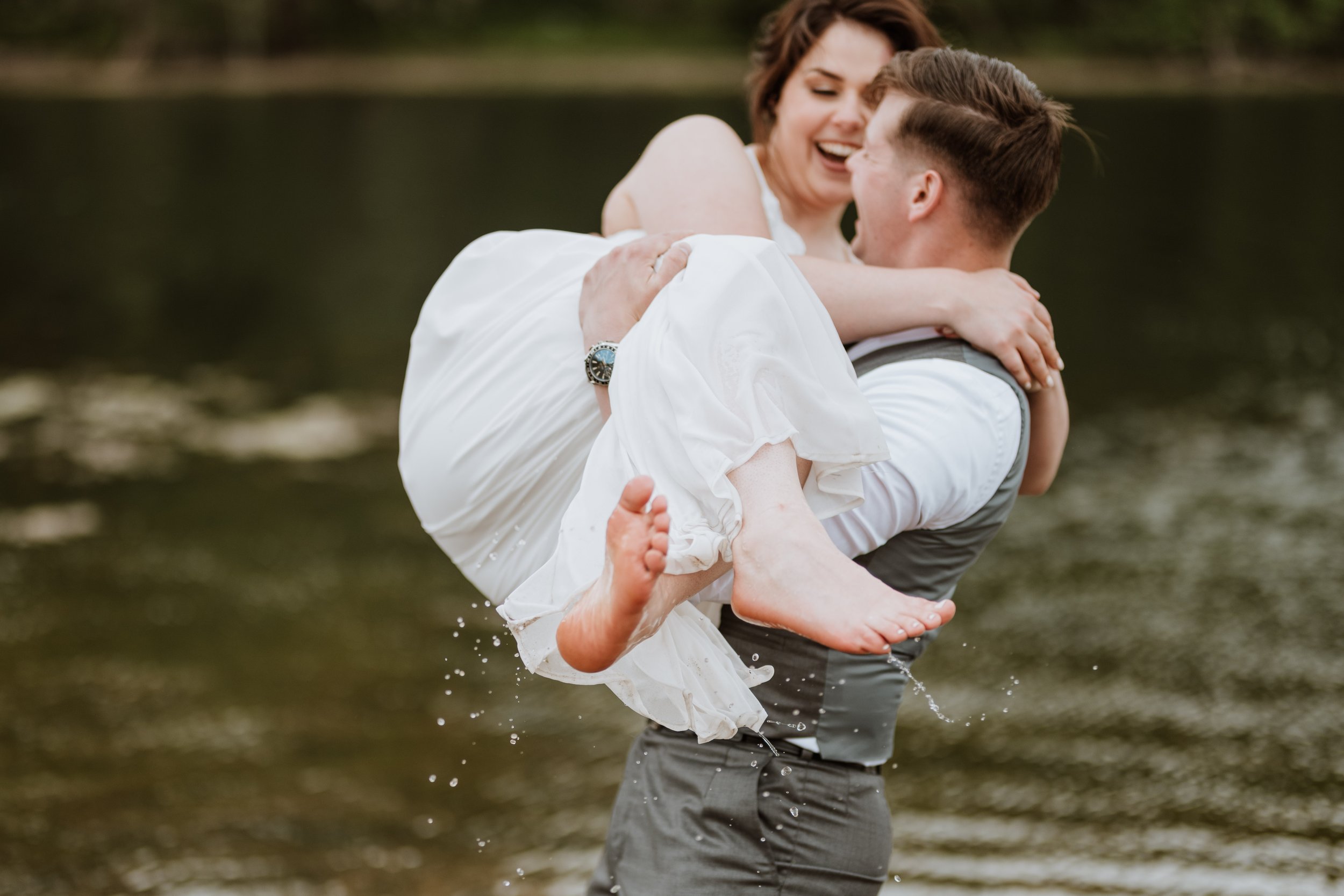 Newlywed groom carrying his wife in a playful manner through water