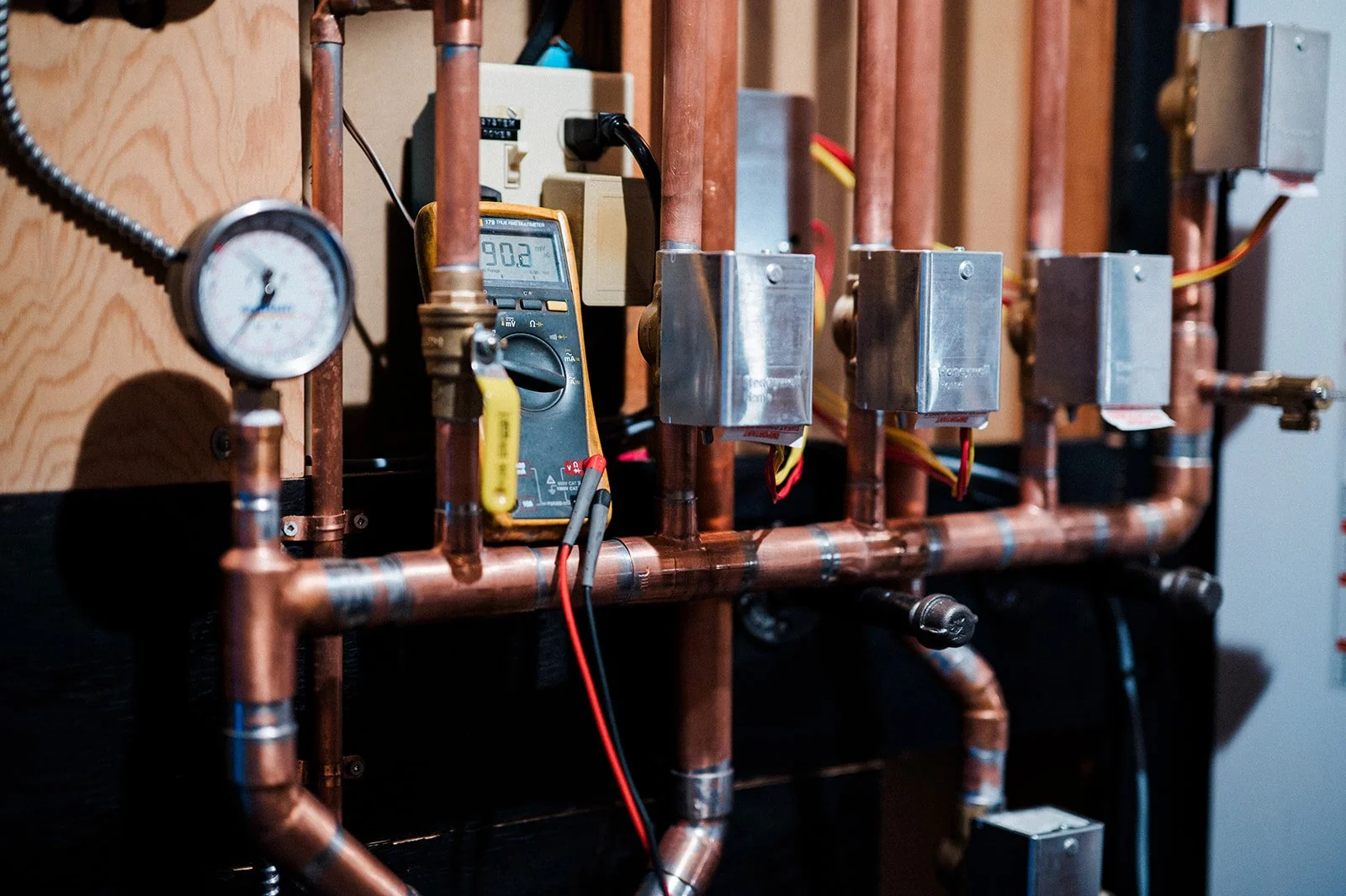 Close-up of copper piping, pressure gauges, electrical controls, and a digital multimeter during mechanical system testing by Maxwell Mechanical.