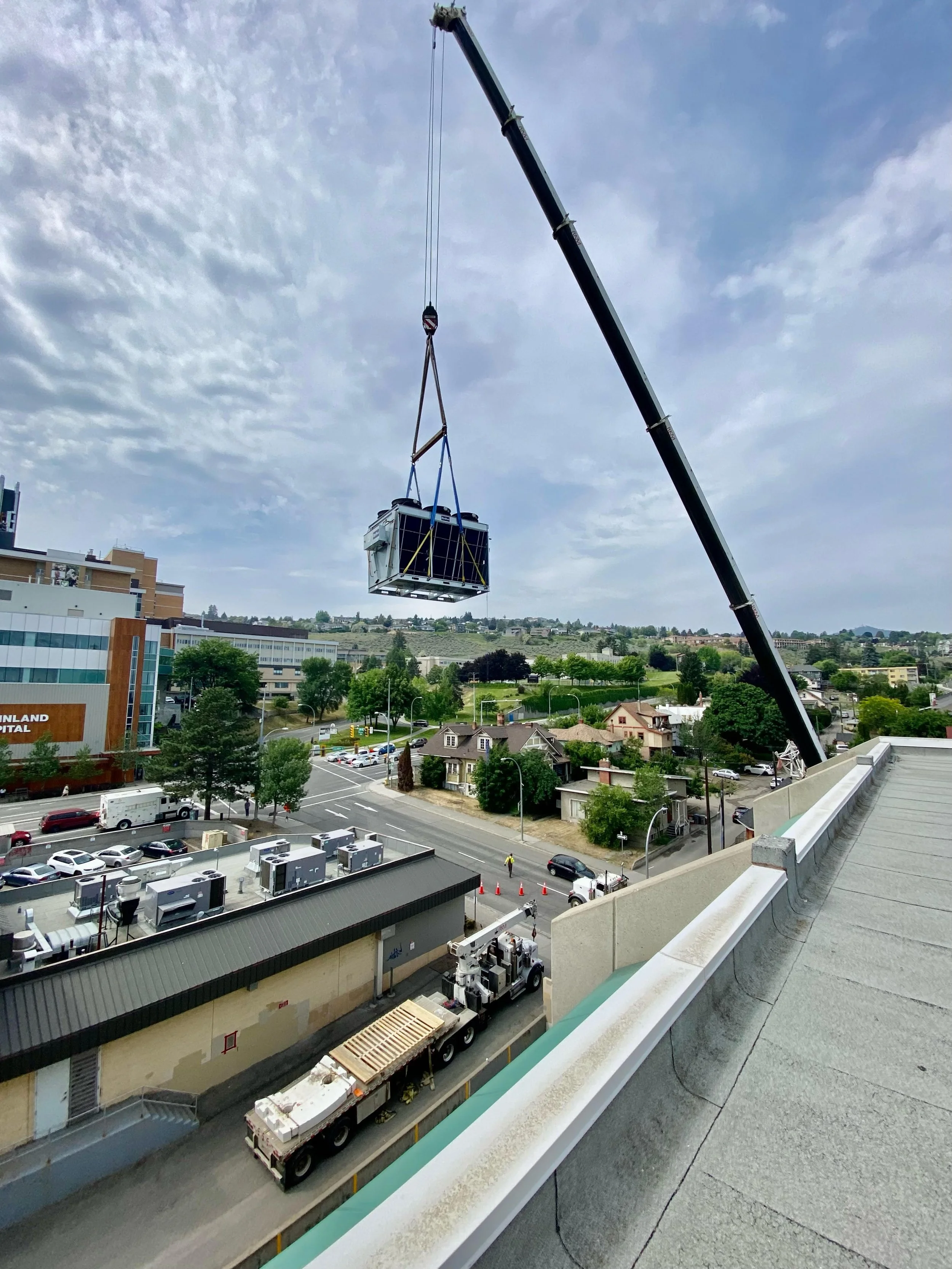 Crane lifting a large commercial HVAC unit onto a rooftop for Maxwell Mechanical installation work.