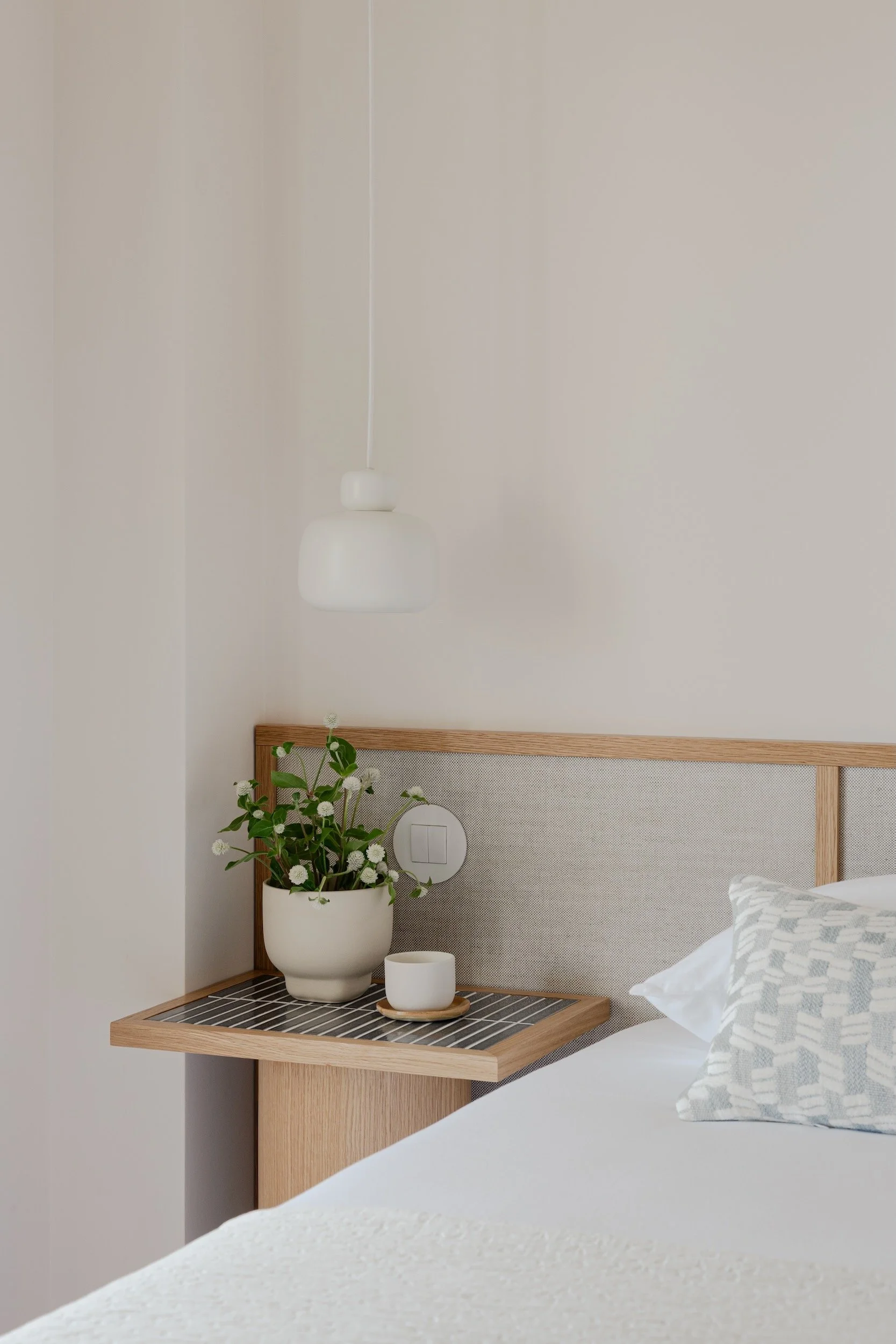 Lola Cwikowski Studio Cascais Residence project with detail of custom Somma Carpintaria oak & linen headboard; nightstand with Marokk Kayo Tokyo tile top; Woud Stone pendant; ceramic planter.