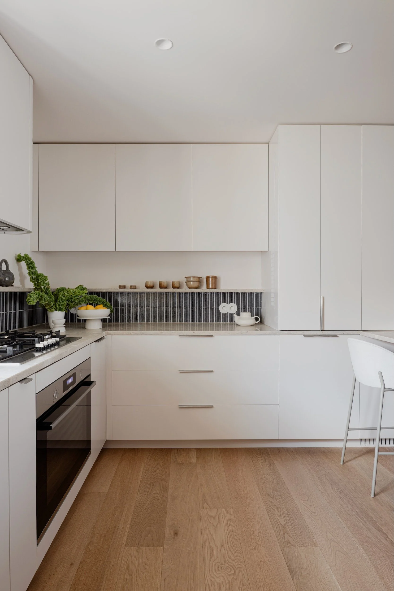 Lola Cwikowski Studio Cascais Residence project with custom white kitchen cabinetry with Lioz countertop; Marokk Kayo Tokyo tile backsplash; oak shelf with ceramics; BoConcept Princeton stool; Bosch oven & hob; Fenesteves oak floor.