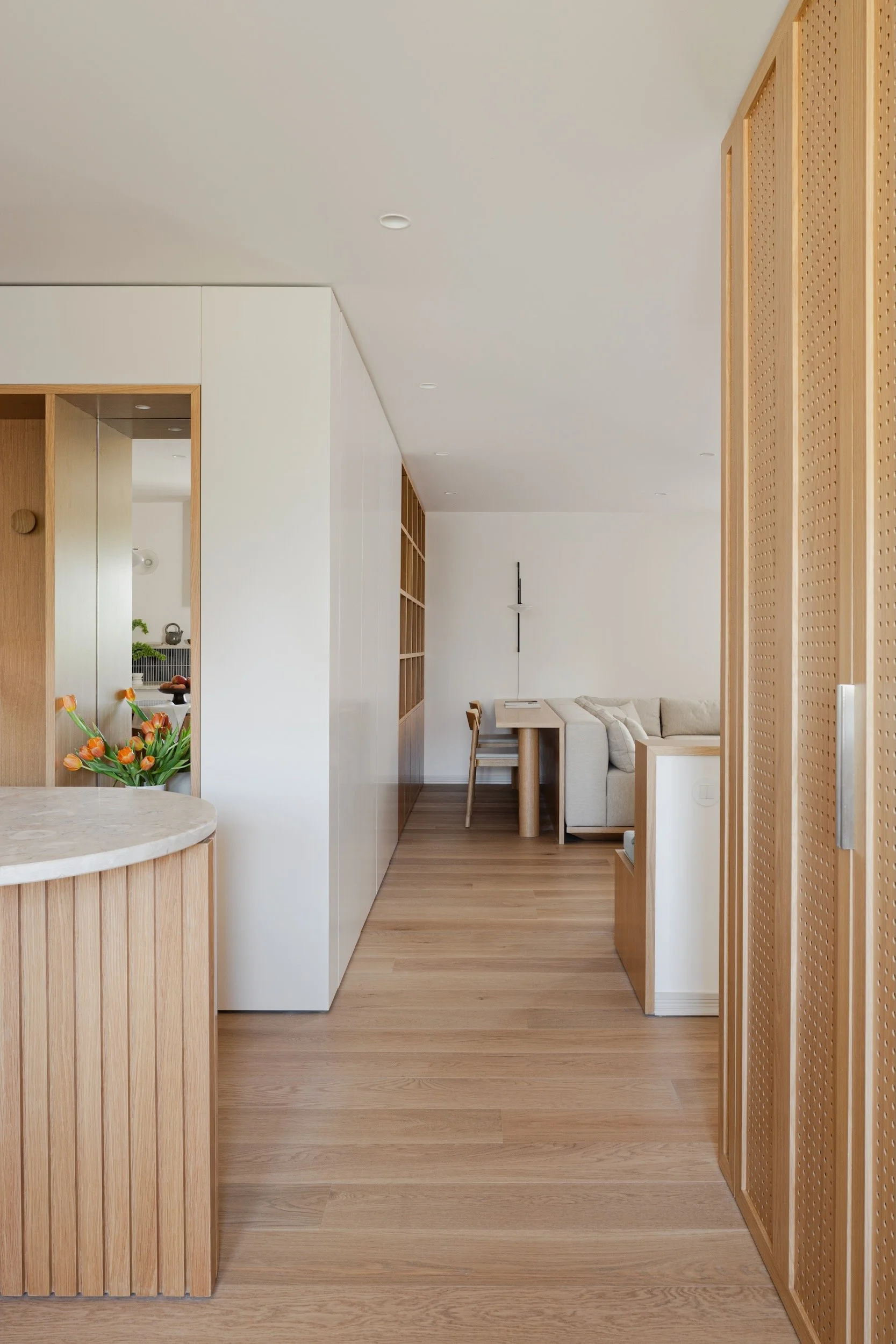 Lola Cwikowski Studio Cascais Residence project with custom perforated oak laundry doors; curved fluted oak island with Lioz countertop; custom oak shelving; Somma Carpintaria sofa and console; Fenesteves engineered oak floor, Vibia Tempo sconce.