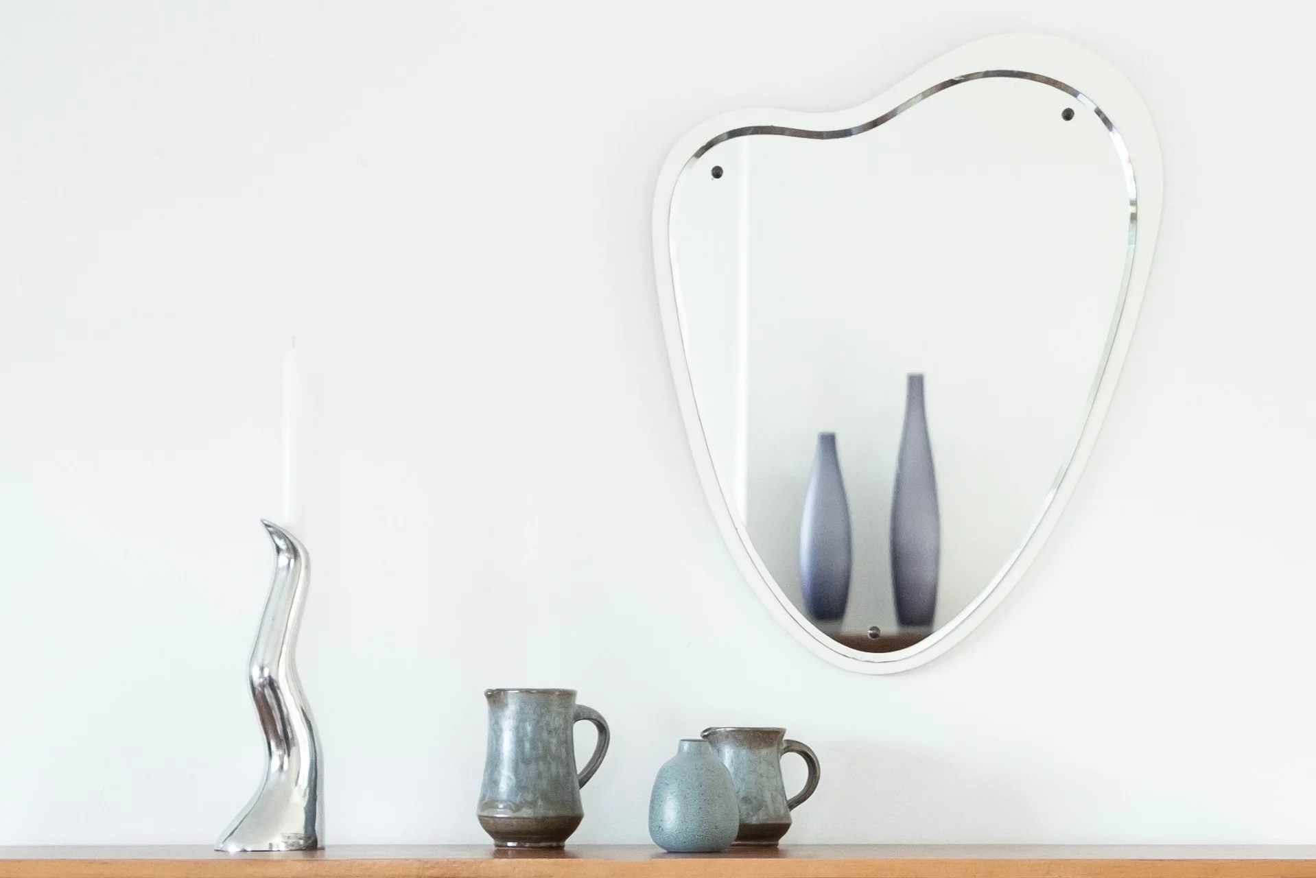 Close up image of silver Anna Efverlund design candle holder and small vases on sideboard with vintage mirror