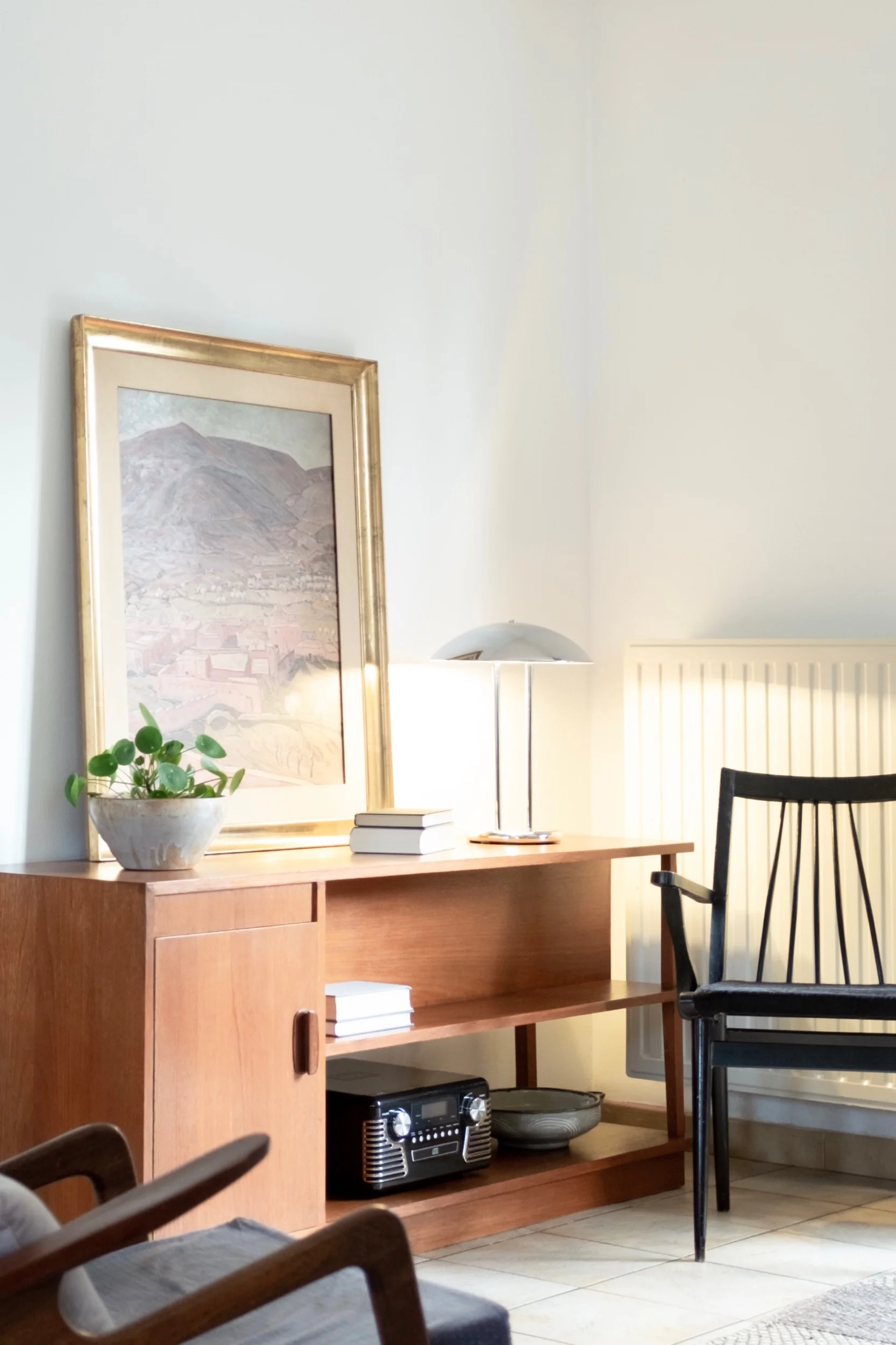 Vintage chromed reading lamp, painting, and pilea plant on wood sideboard