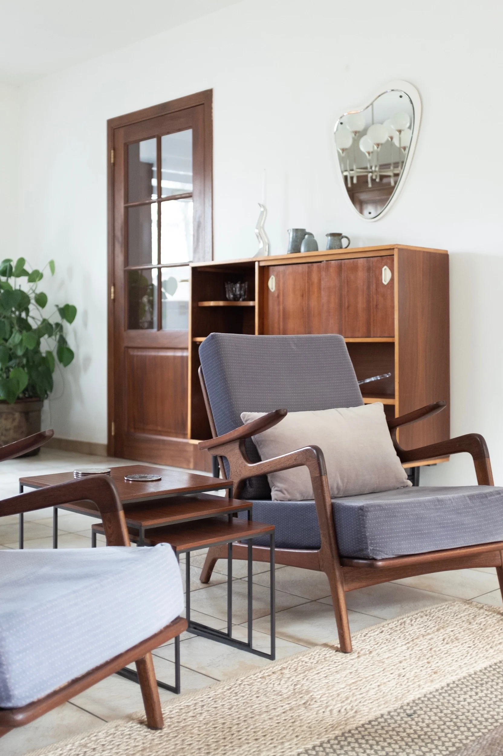 Vintage armchair and nesting tables in front of restored wooden sideboard and organic shape mirror