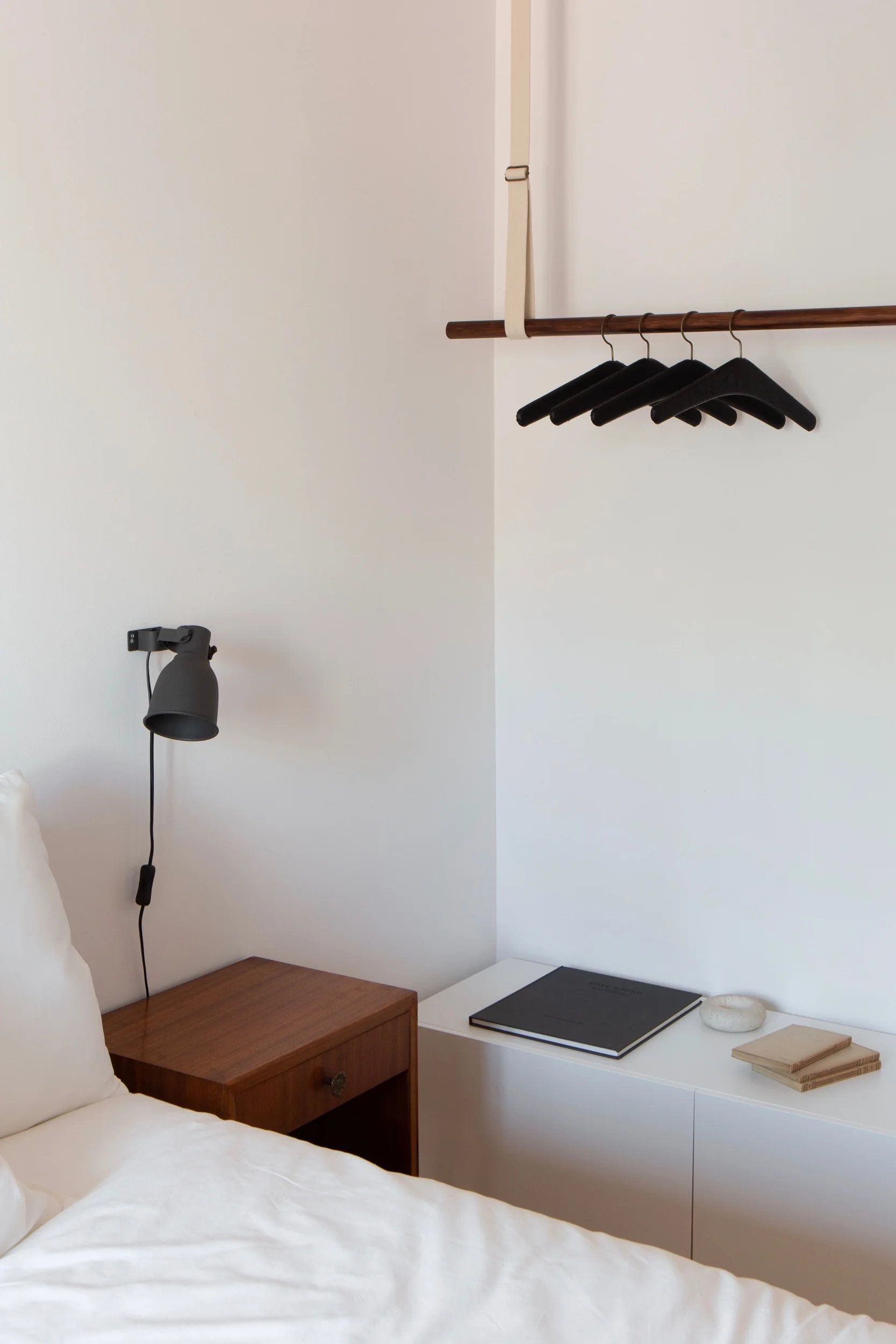 Detail photo of Lola Cwikowski Studio Travessa da Pereira Apartment residential project showing bedroom with vintage nightstands and custom clothes hanging system with vintage black leather hangers.