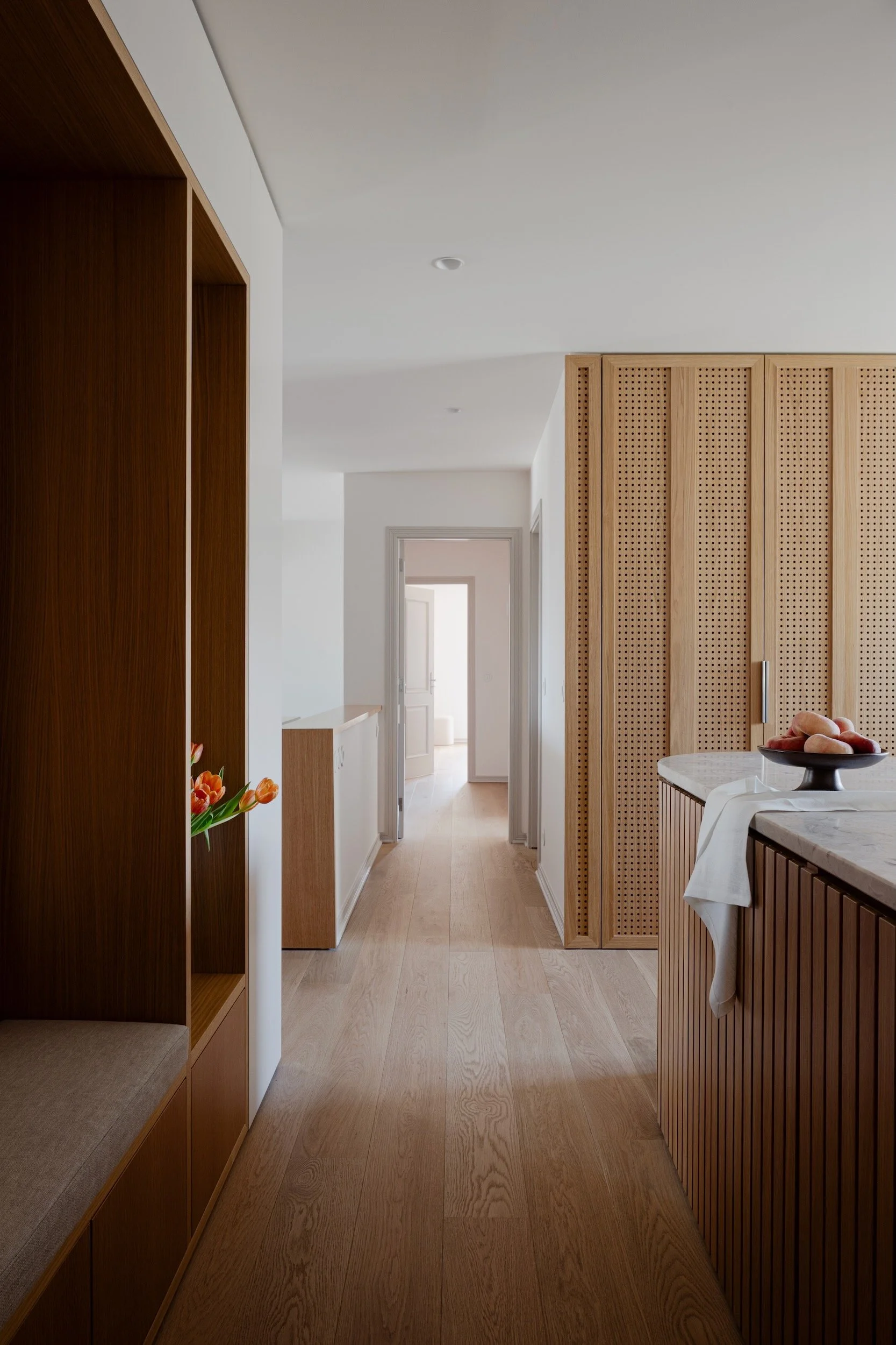 Lola Cwikowski Studio Cascais Residence project with custom oak entry bench & niche with tulips; perforated oak laundry doors; curved fluted oak island with Lioz countertop; Fenesteves engineered oak floor.