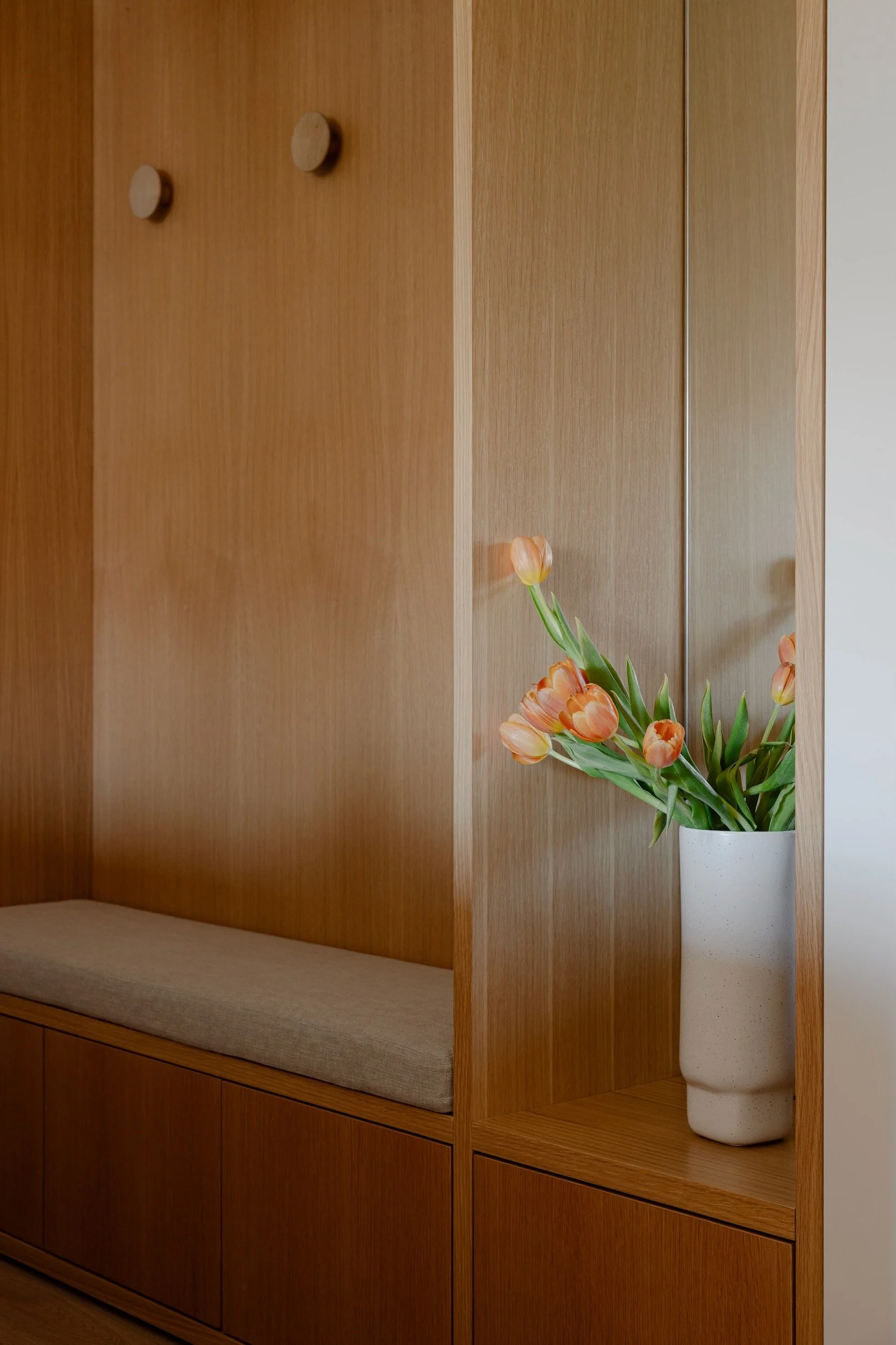 Lola Cwikowski Studio Cascais Residence project with detail of custom oak entry bench, Maria Menino cushion in Lauritzon Aqua; Muuto Dots Wood oak hooks; vintage ceramic vase with tulips; oak veneer paneling.