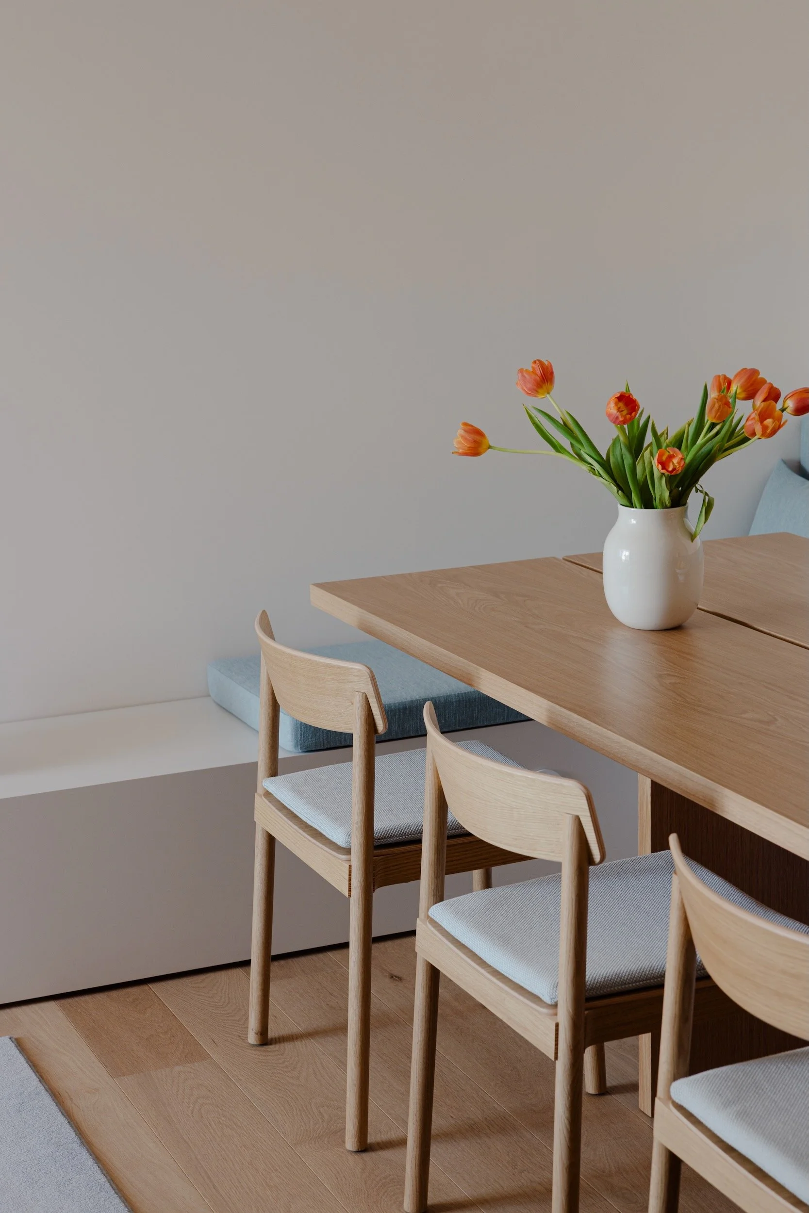 Lola Cwikowski Studio Cascais Residence project with custom Somma Carpintaria oak dining table; &Tradition Betty TK2 chairs with Maharam Merit cushions; Maria Menino bench cushions in Lauritzon Aqua; ceramic pitcher with tulips.