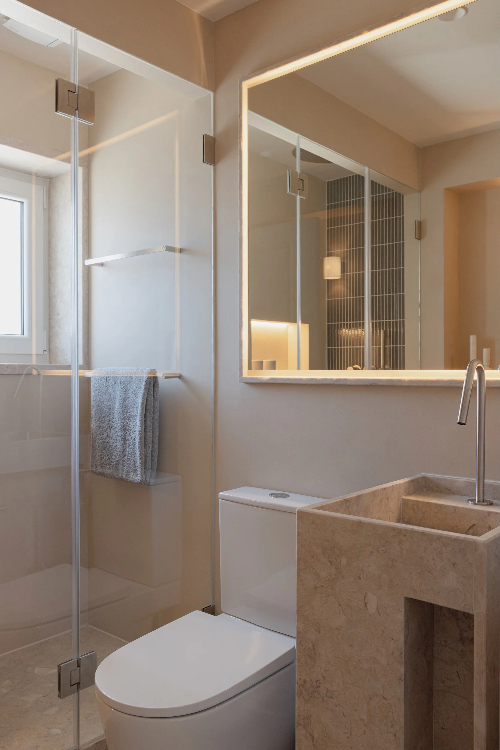 Lola Cwikowski Studio Cascais Residence project with custom Lioz pedestal sink; Lioz-framed backlit mirror with Brilumen LED; Roca toilet; Bruma X-Alpha tapware; glass shower screen; Lioz stone floor.