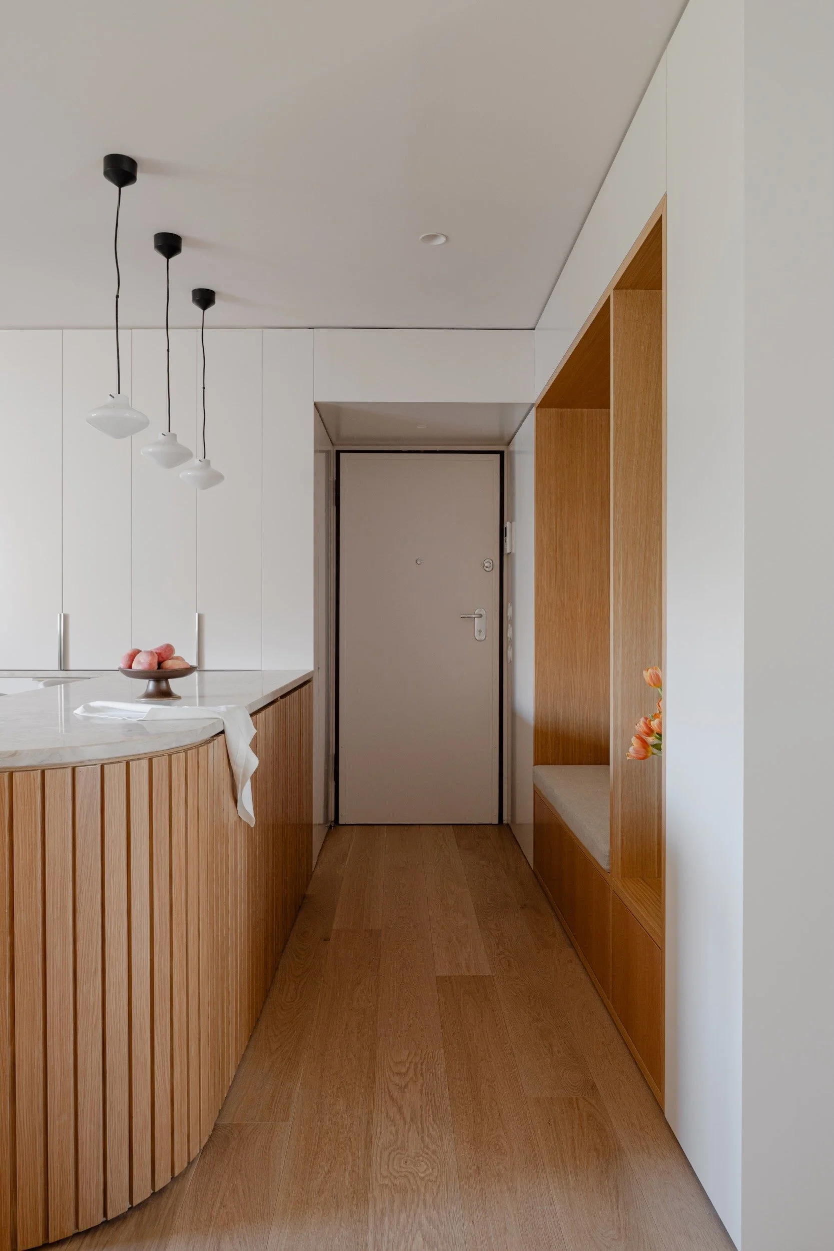Lola Cwikowski Studio Cascais Residence project with custom curved fluted oak kitchen island with Lioz countertop; Lyfa Repose pendants; custom oak entry bench & niche; footed fruit bowl; Fenesteves engineered oak floor.