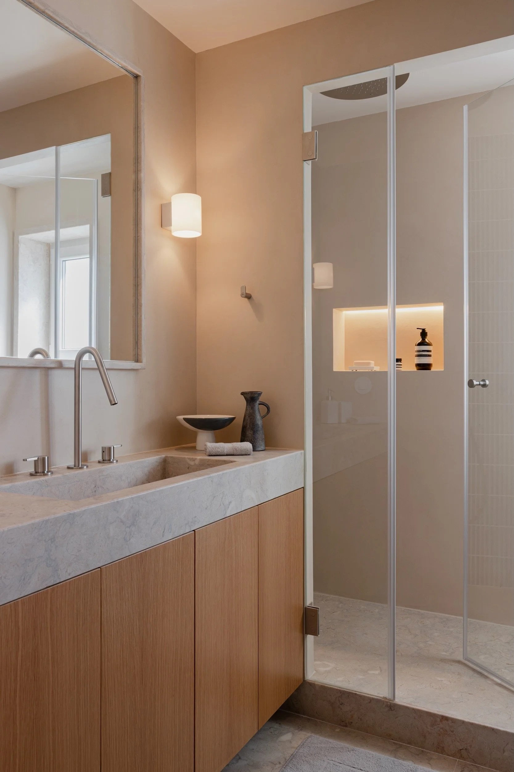 Lola Cwikowski Studio Cascais Residence project with custom Lioz countertop with integrated sink; oak vanity; Lioz-framed mirror; Bruma X-Alpha tapware; Herstal Evoke sconce; ceramic bowl; Lioz stone floor.