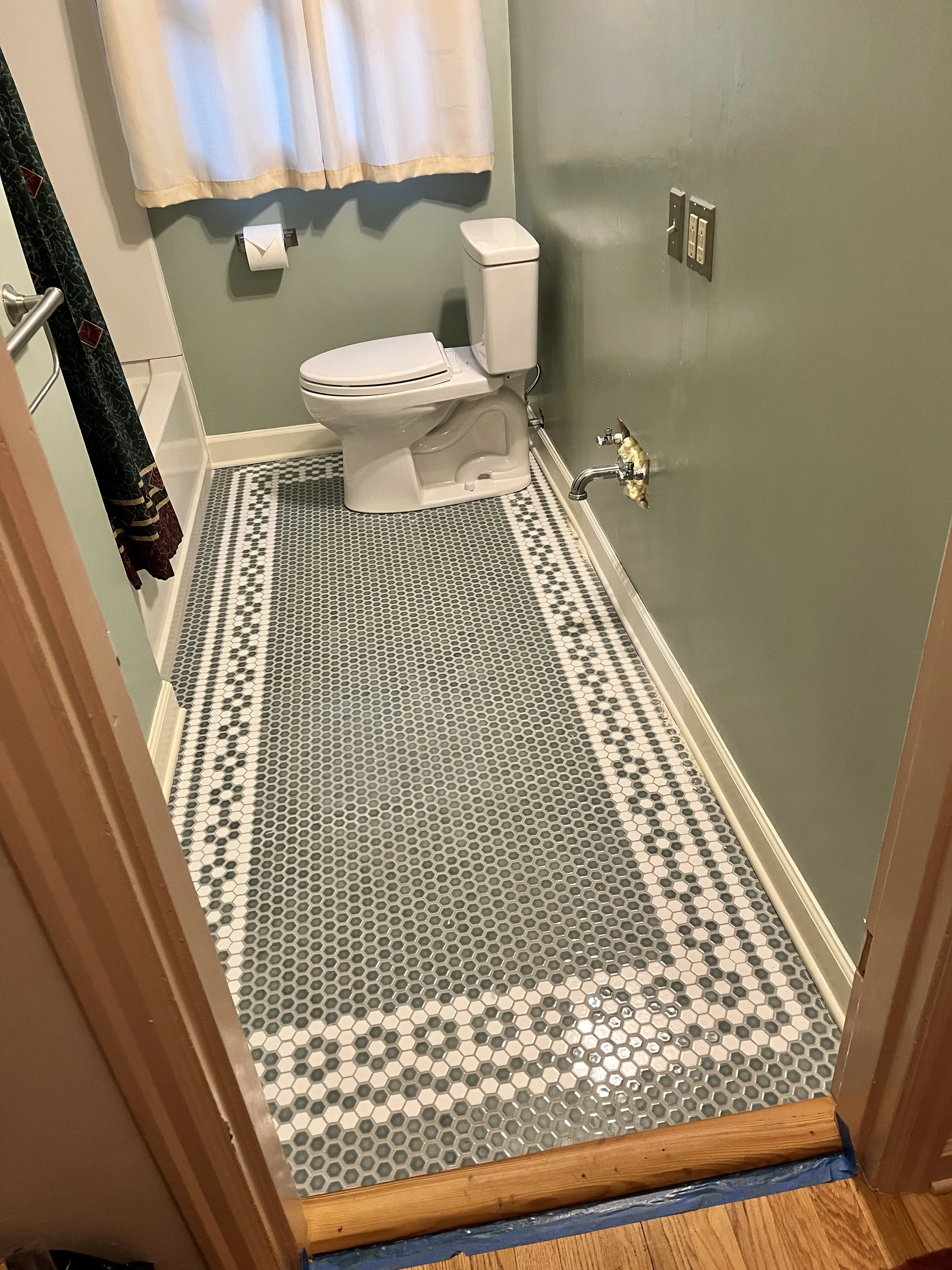 Period-style hex tile bathroom floor installation in a 1940s SE Portland home featuring a custom mosaic border.