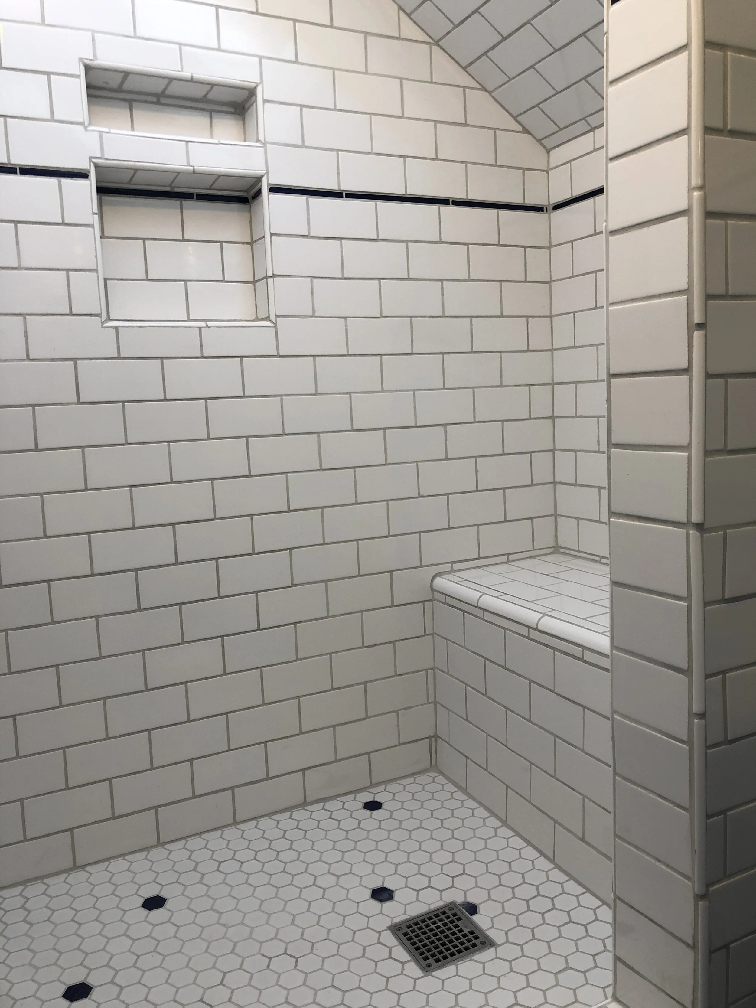 Custom walk-in shower with white subway tile, hex tile floor, built-in niches, and tiled bench seat in a Portland bathroom remodel