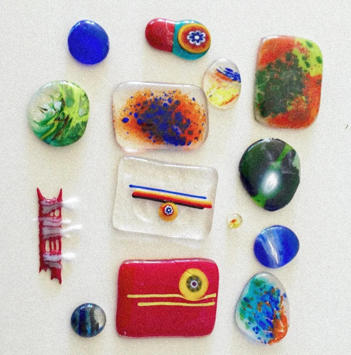 Conjunto de peças de vidro coloridas e decoradas, incluindo bolinhas, quadrados, e formas variadas, com padrões e cores vibrantes.