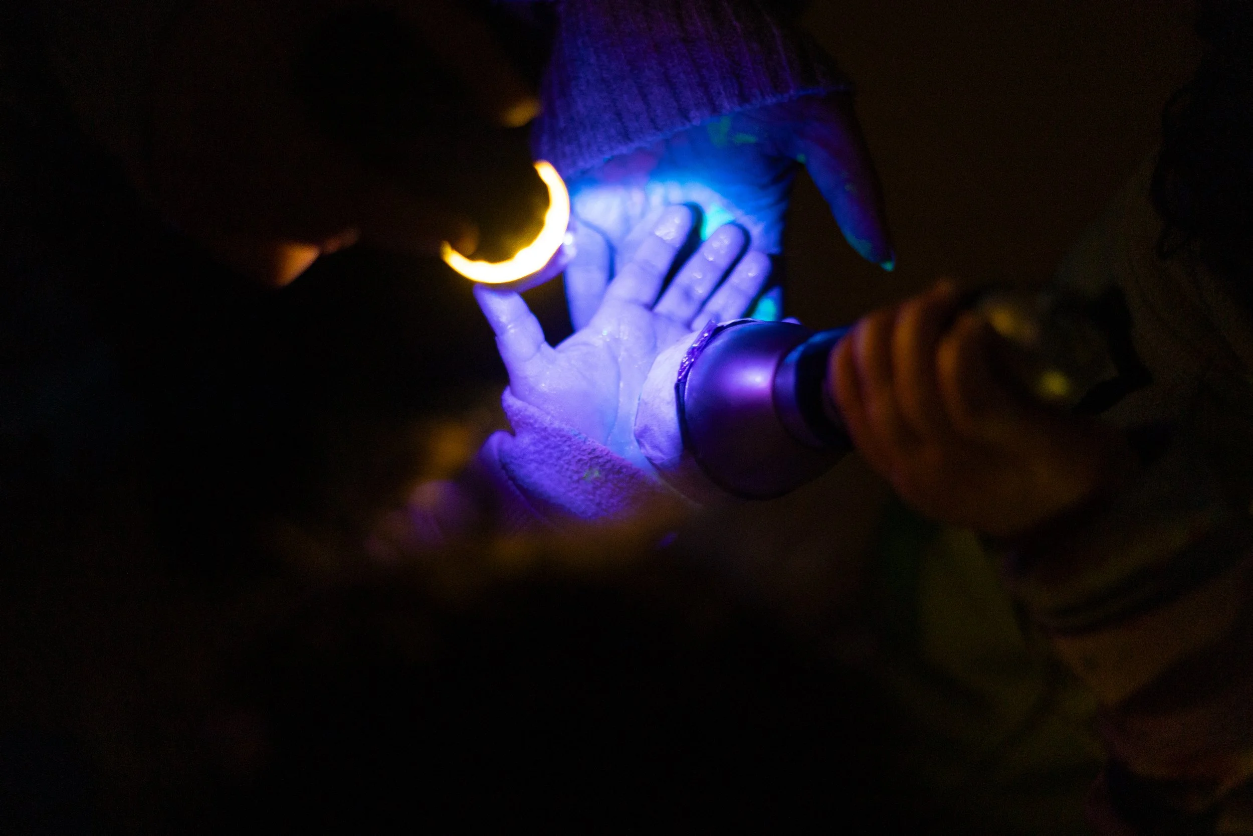 Pessoa usando uma luva que brilha no escuro, tocando uma superfície com uma luz negra, criando efeito de iluminação azul e roxa.