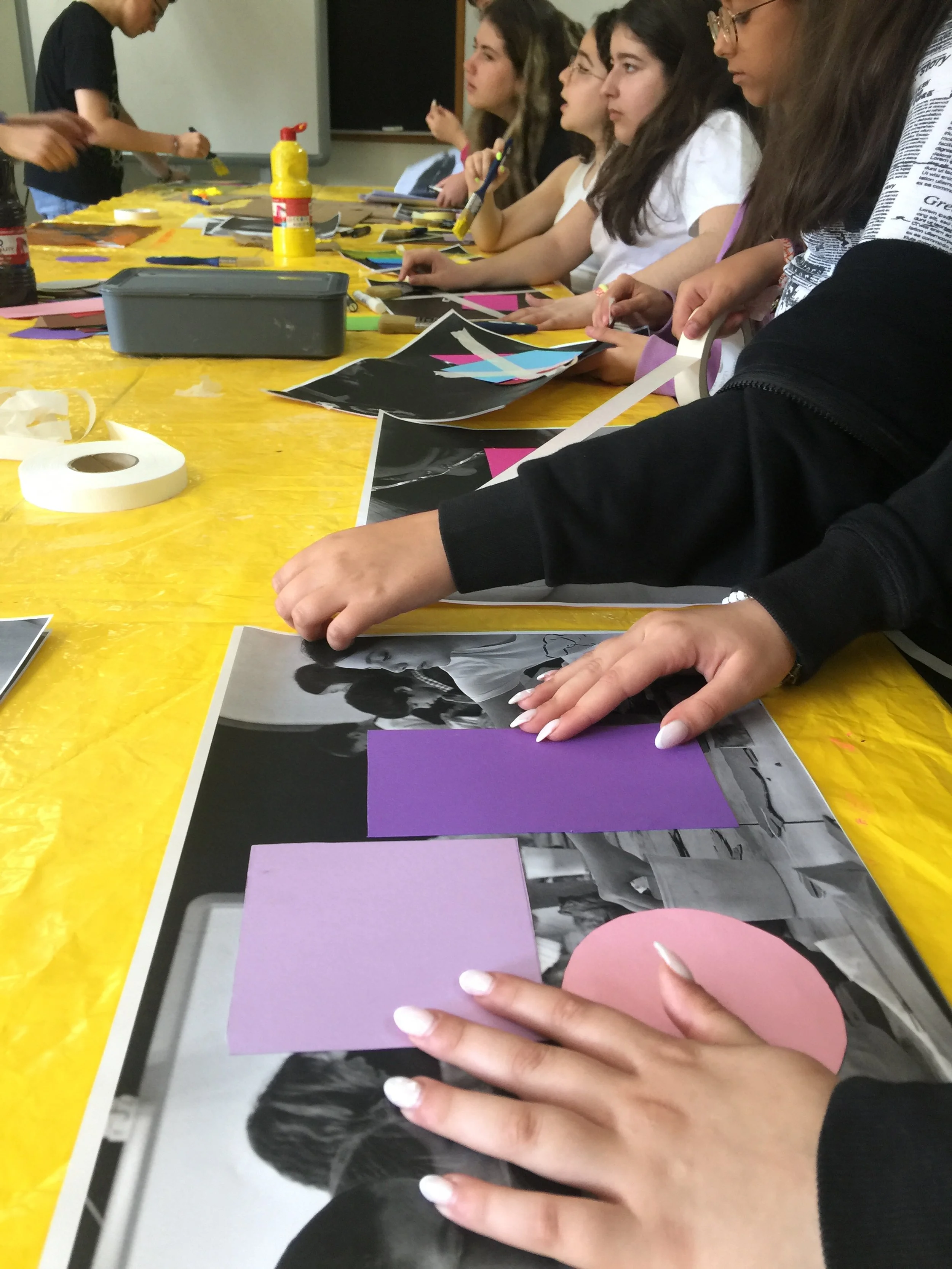 Pessoas fazendo colagem com recortes coloridos em uma mesa, participando de uma atividade artística.