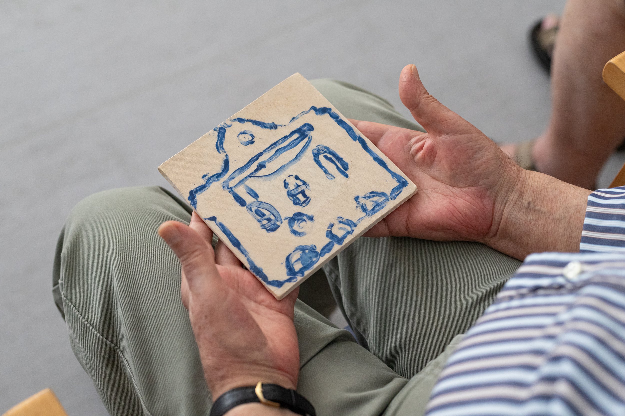 Pessoa segurando uma peça de cerâmica com desenho de uma casa azul.