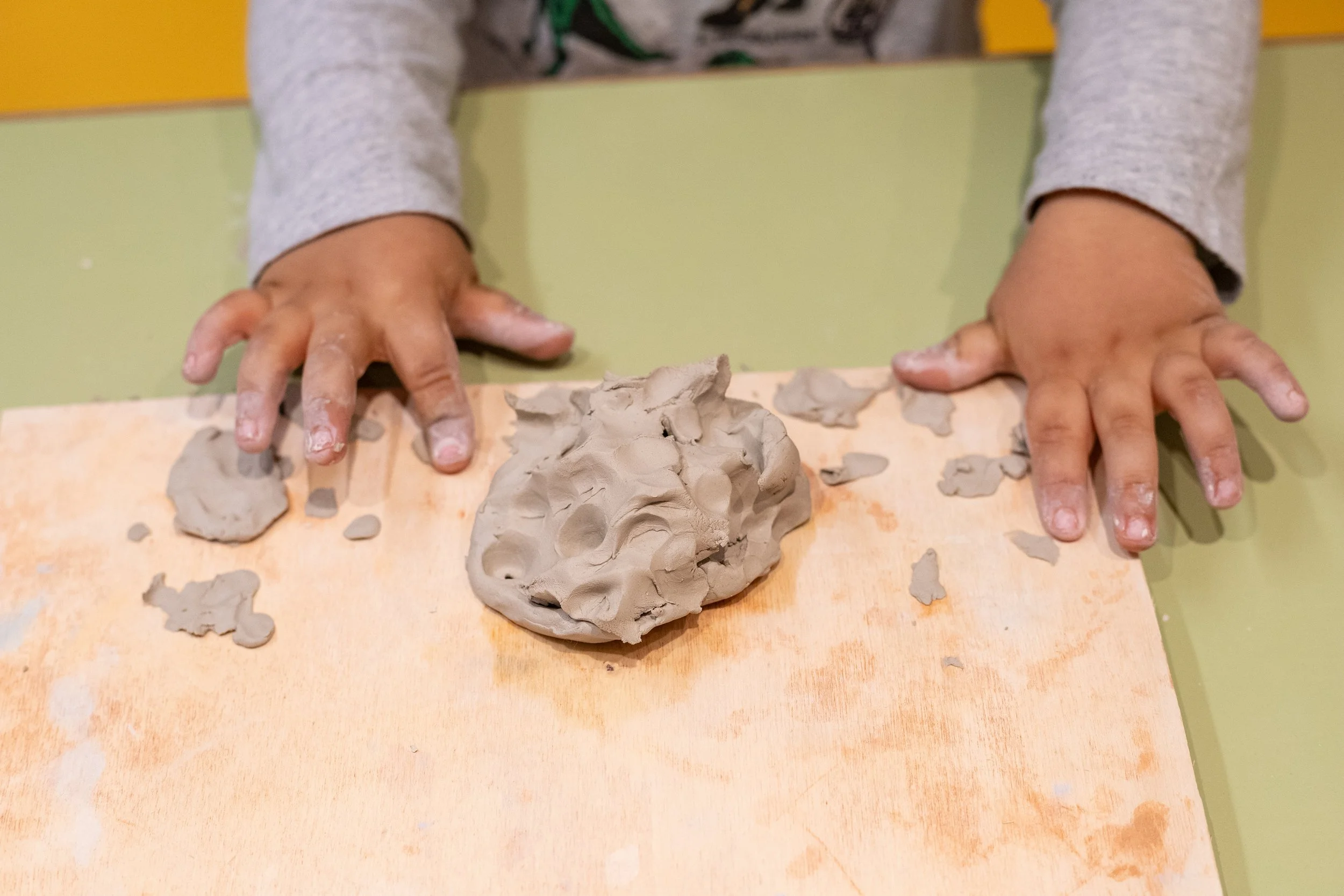 Criança brincando com massa de modelar cinza em uma mesa de cor clara.