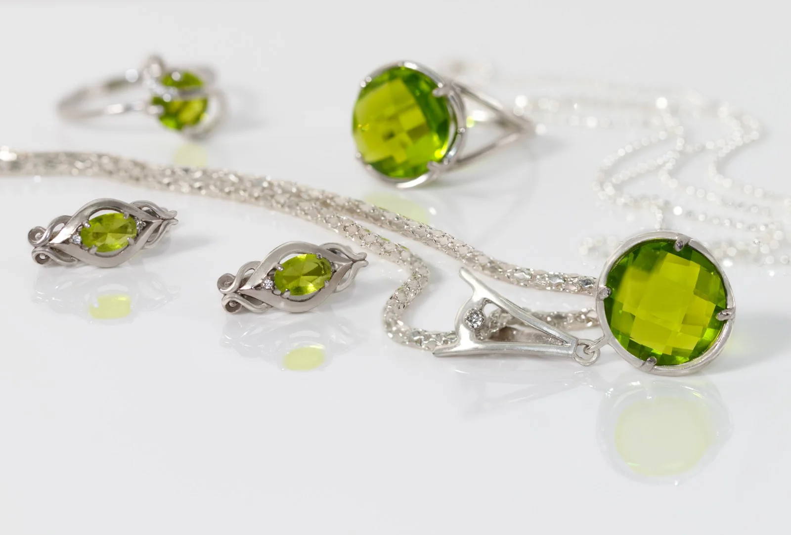 Close-up beauty silver pendant, earrings with peridot on background chain and rings on white acrylic desk.