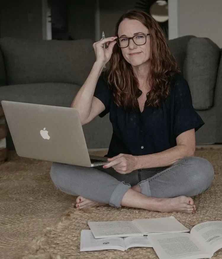 Jessica Uys seated on a rug with a laptop, adjusting her glasses.