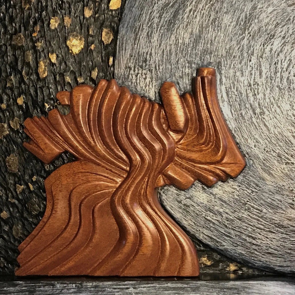The dancing figure is carved from mahogany with several coats of varnish to allow the figure to shine. The moon is shaped from a found laminated maple cutting board, textured, layered with teak oil and oil paint stain, and finished with silver metallic wax. The curved shape that the figure dances upon is basswood with the same finish as the moon. The background represents the cosmos and is from a found piece of wood that had the long beveled sides in its original form. I textured the surface and gave it a dark umber/black oil stain, highlighting the "stars" with gold leaf. My hope with this piece, is that the viewer will be reminded to take time to dance and celebrate...a lot...while we are on this earth. It is really only a brief time in the long view.