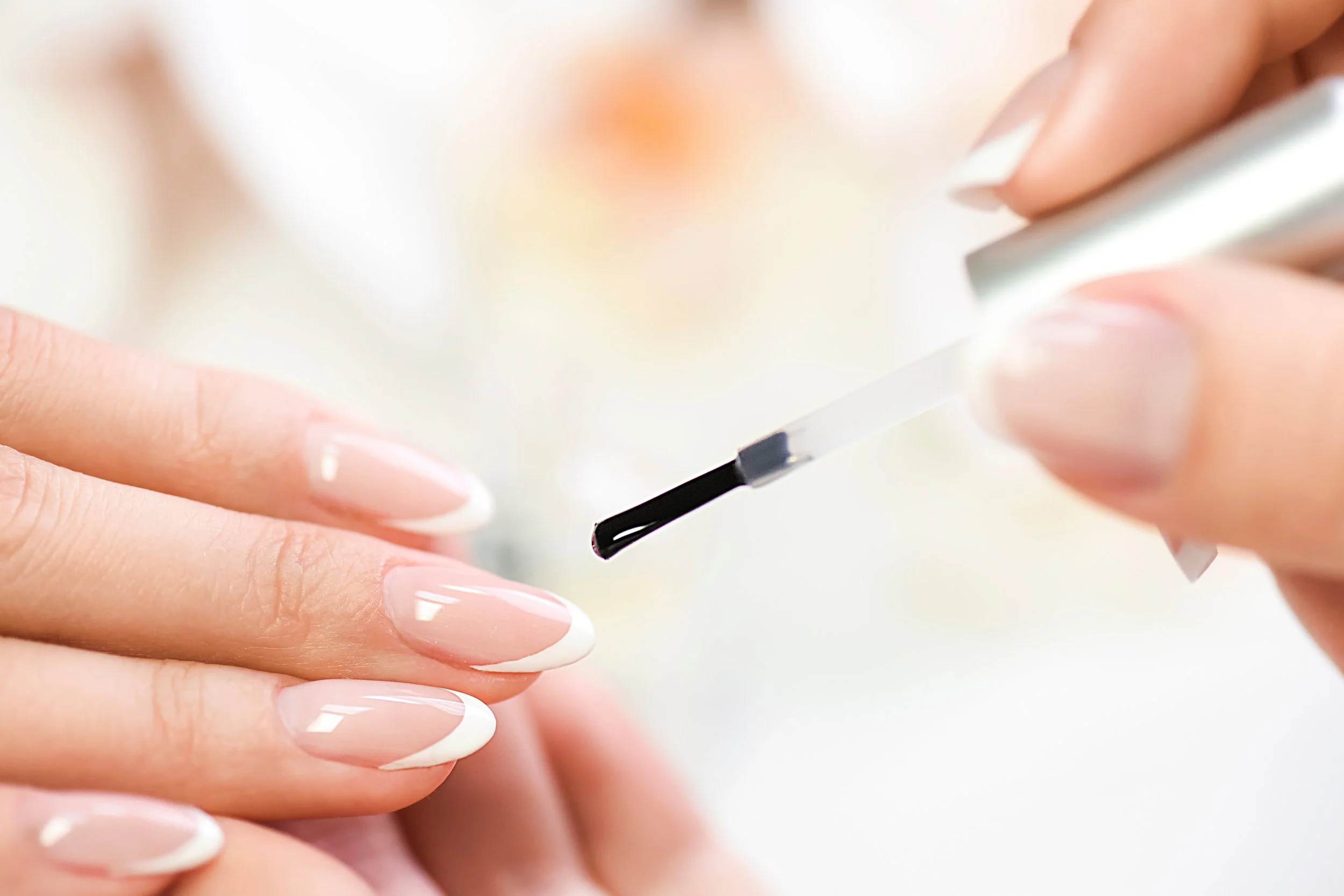 Close-up of a person applying clear nail polish with a brush to their fingernails.